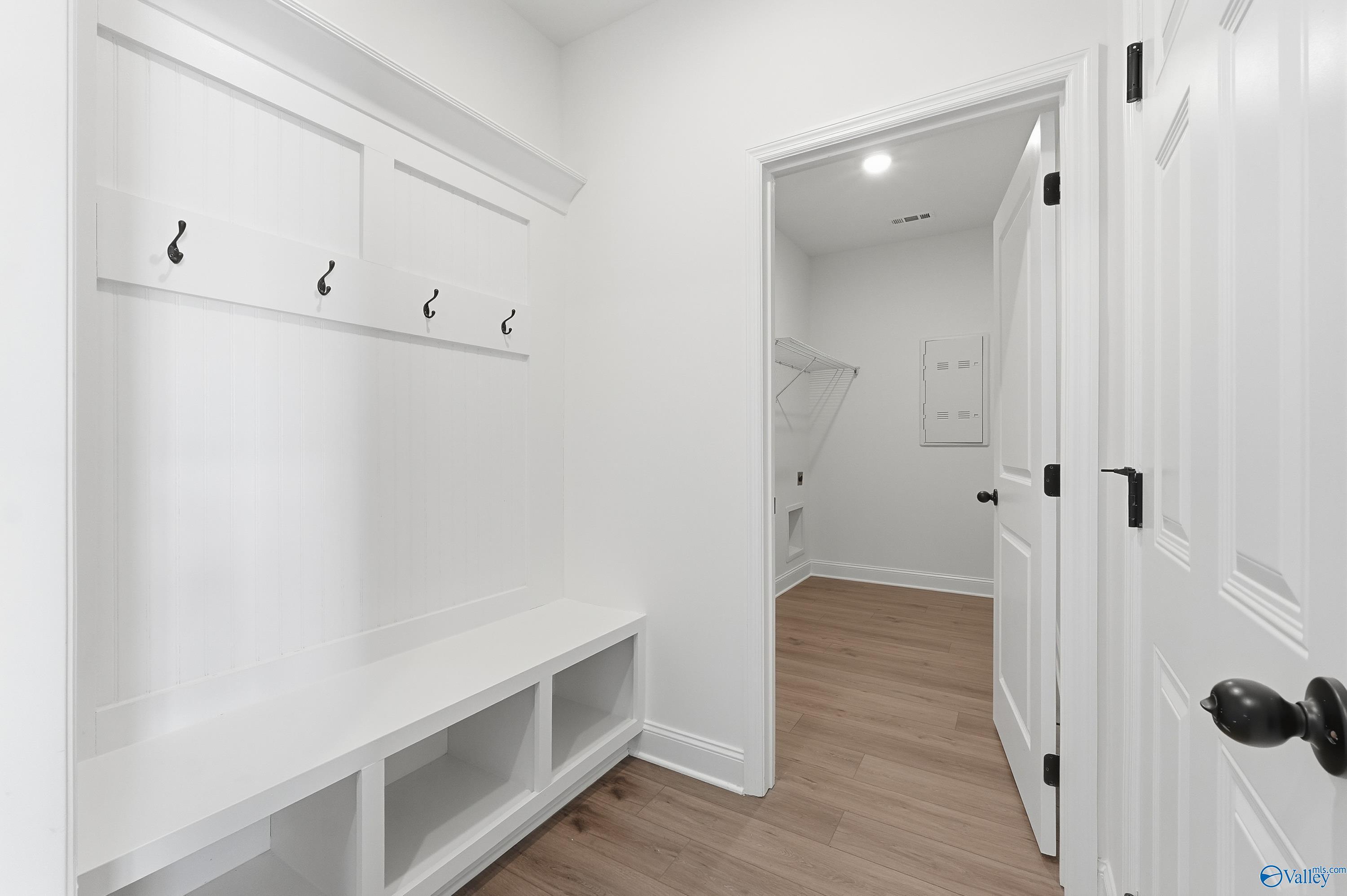 Bright white mudroom with built-in bench, coat hooks, open shelving, and laundry area in Davidson Homes The Rockford D, Hazel Green, Alabama