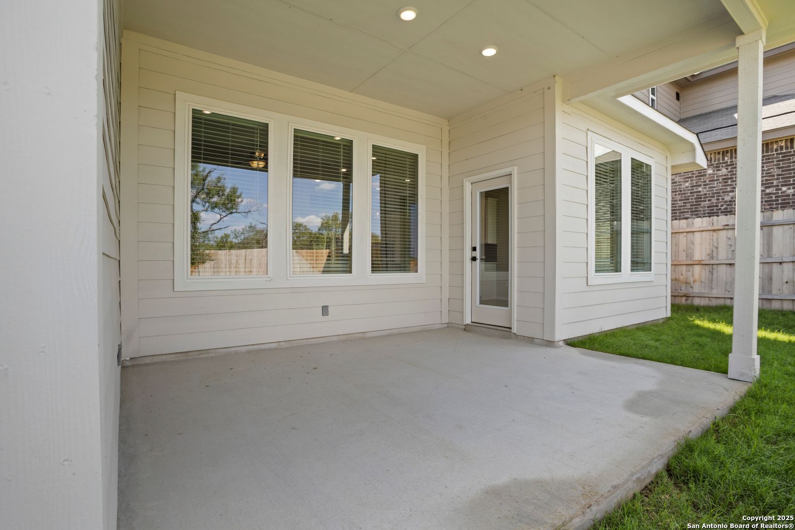 Covered back patio with large windows, concrete floor, and lush lawn in Davidson Homes The Sequoia A, Converse, Texas