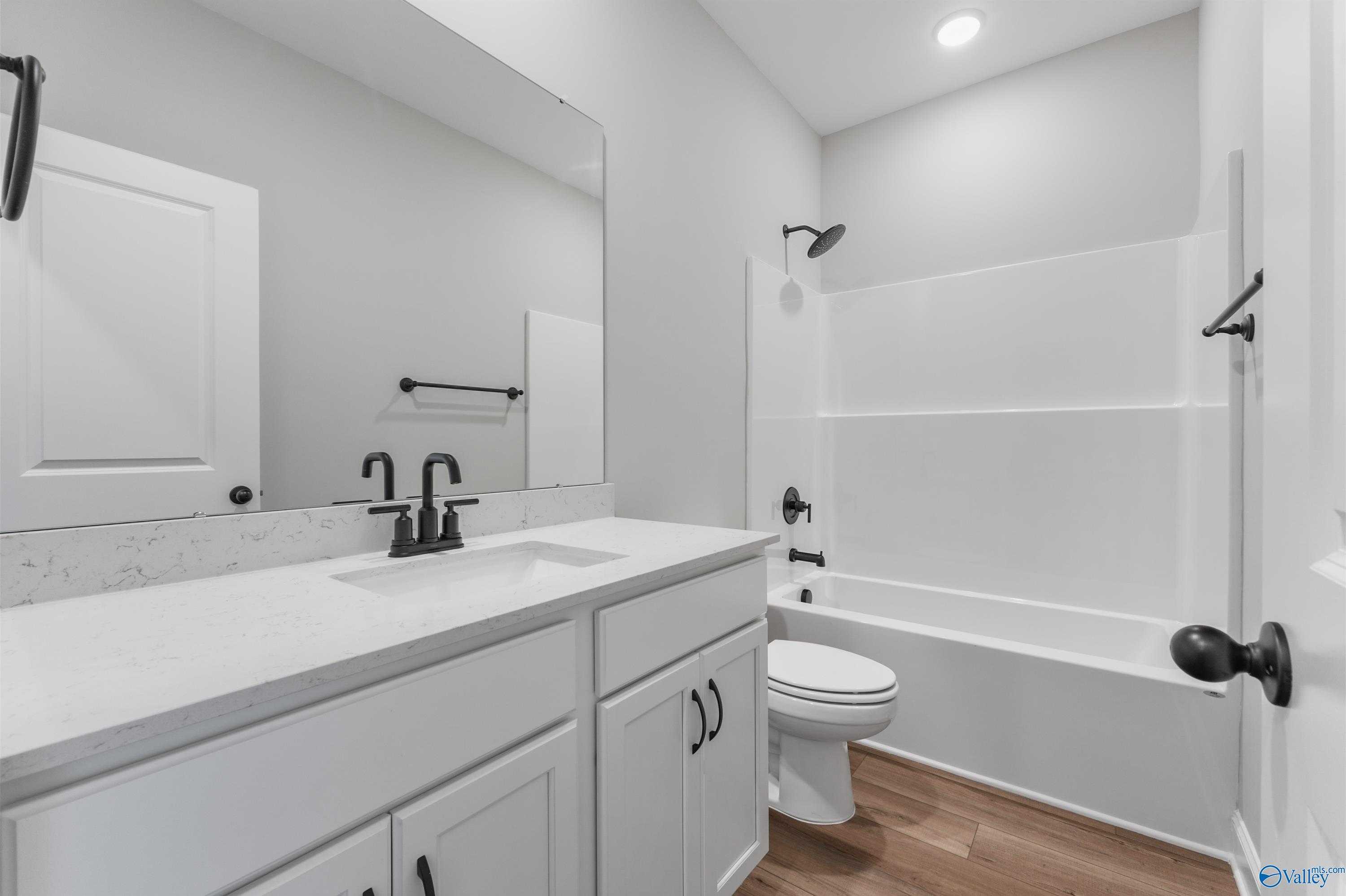 Modern bathroom with white quartz vanity, single sink, tub-shower combo, and black fixtures in The Daphne C, Hazel Green AL