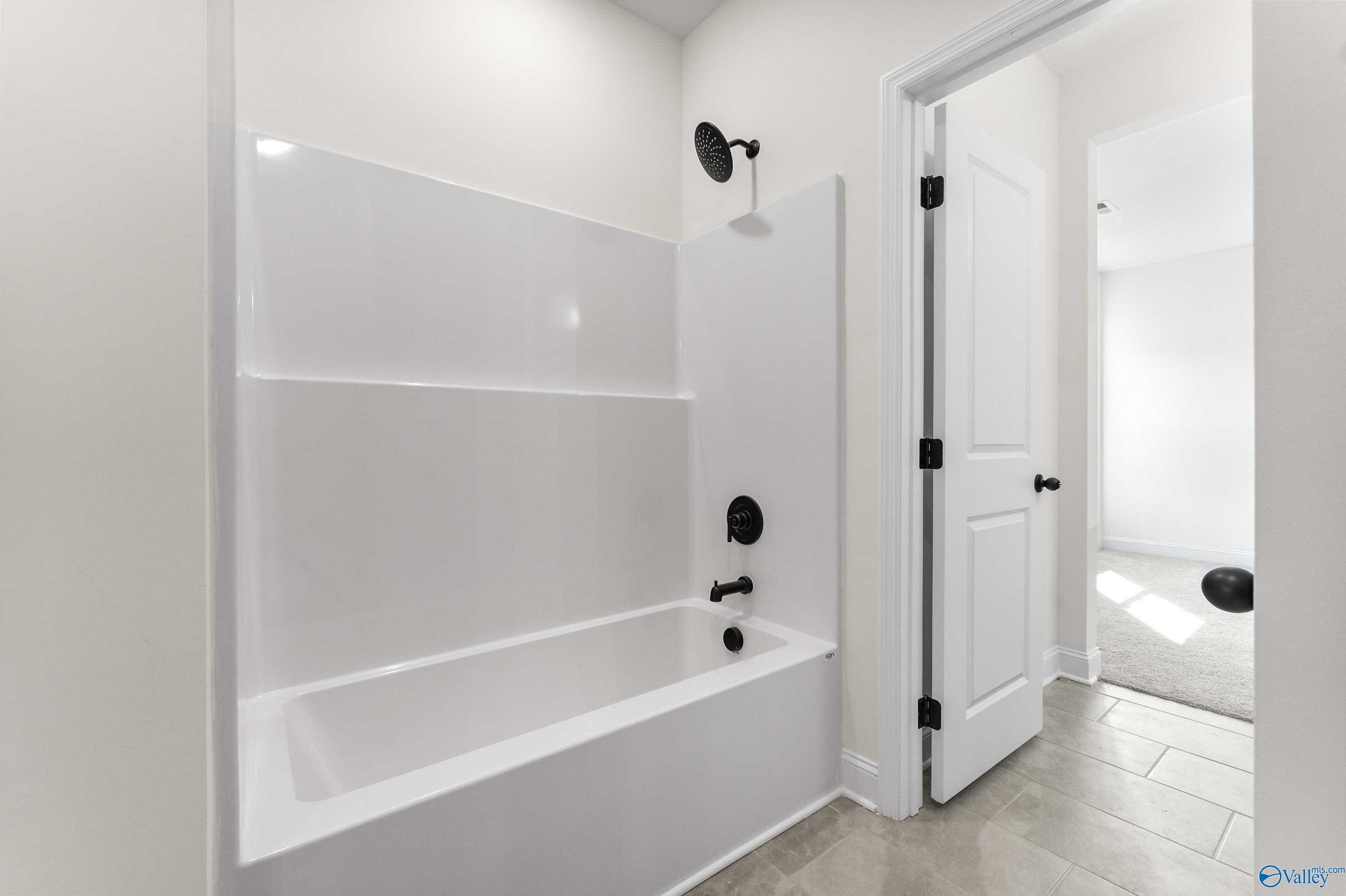 Bright white bathtub and seamless shower with black fixtures in modern bathroom, The Finleigh by Davidson Homes, Harvest AL