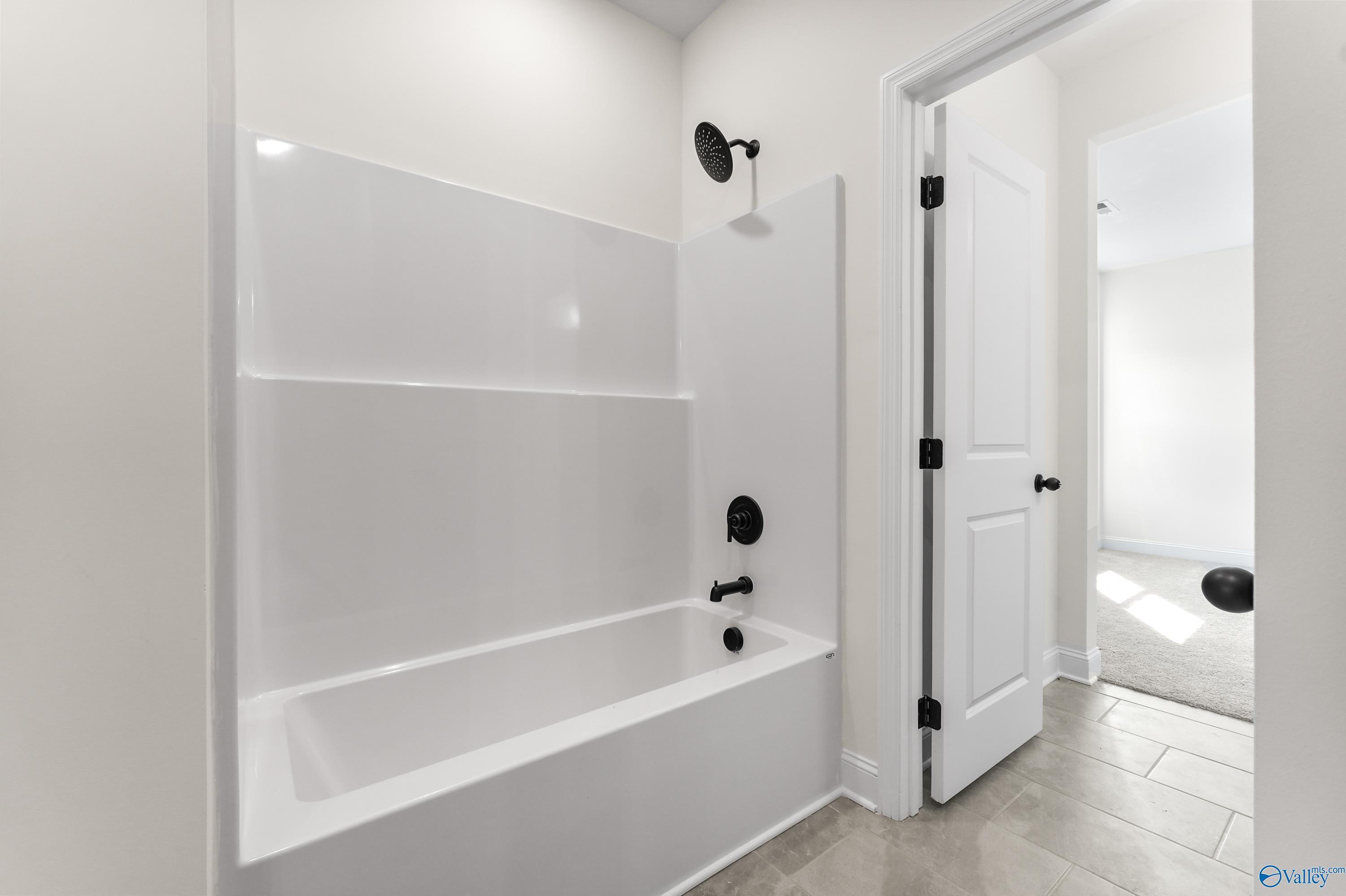 Bright white bathtub and seamless shower with black fixtures in modern bathroom, The Finleigh by Davidson Homes, Harvest AL