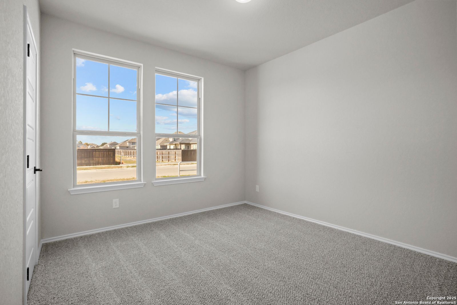 Bright bedroom with light gray walls, neutral carpet, and large windows overlooking neighborhood in The Daphne H, Hannah Heights, Seguin, Texas