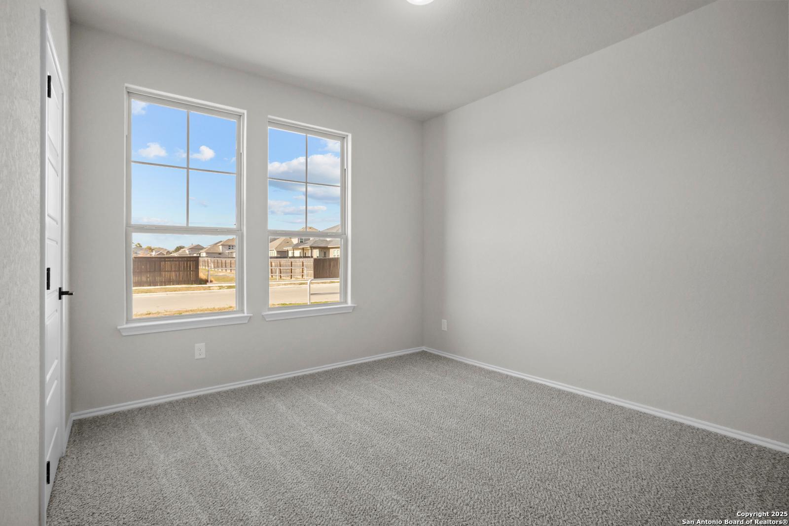 Bright bedroom with light gray walls, neutral carpet, and large windows overlooking neighborhood in The Daphne H, Hannah Heights, Seguin, Texas