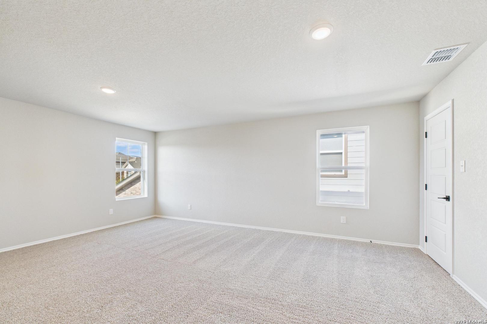 Empty bedroom with beige walls, carpeted floor, and large windows in Davidson Homes The Douglas E, Bricewood, San Antonio