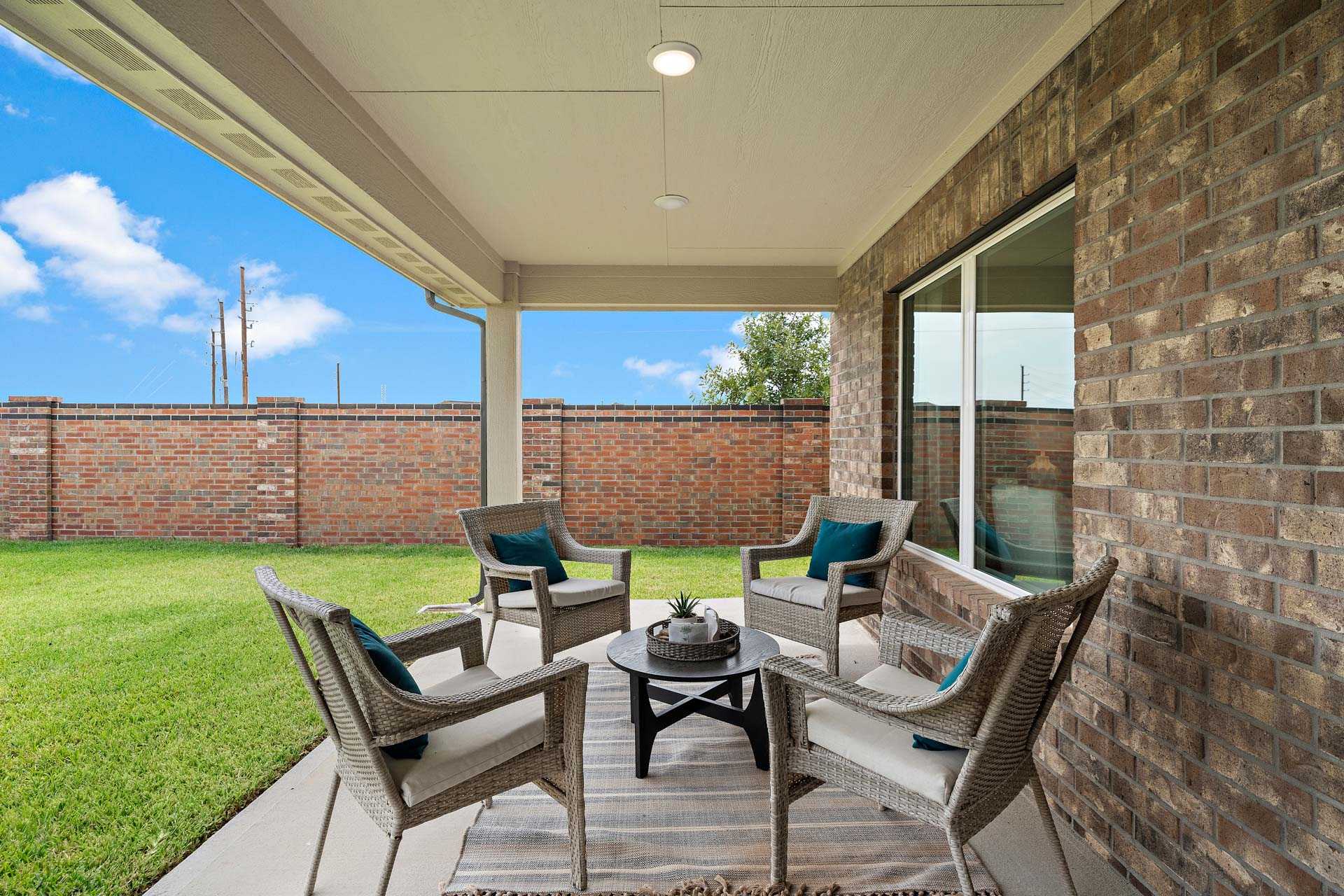 Covered patio at Sunterra in Katy Texas by Davidson Homes with wicker seating lush lawn and brick exterior