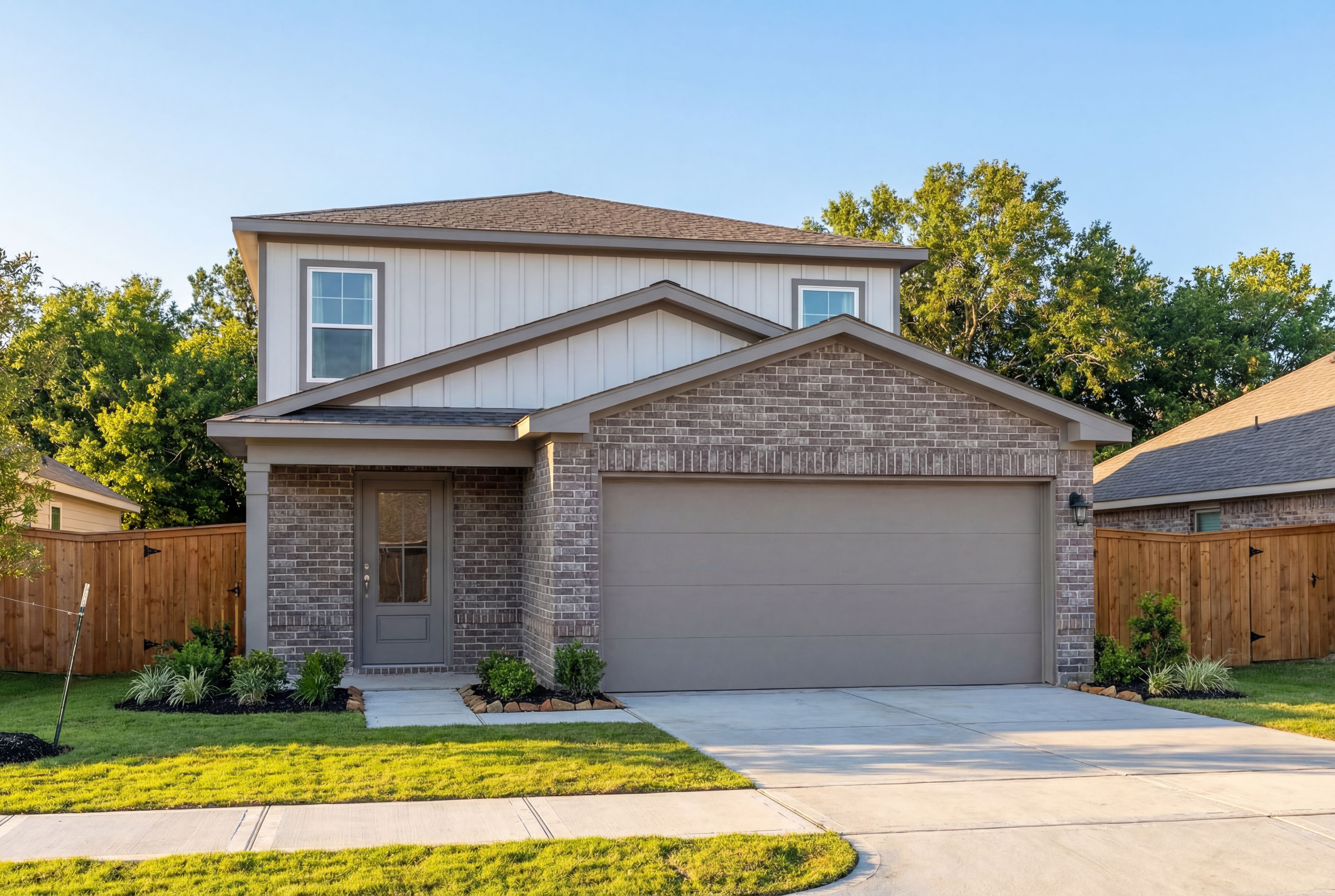 Modern two-story The San Marcos home exterior with brick and siding, two-car garage, front porch, and lush landscaping