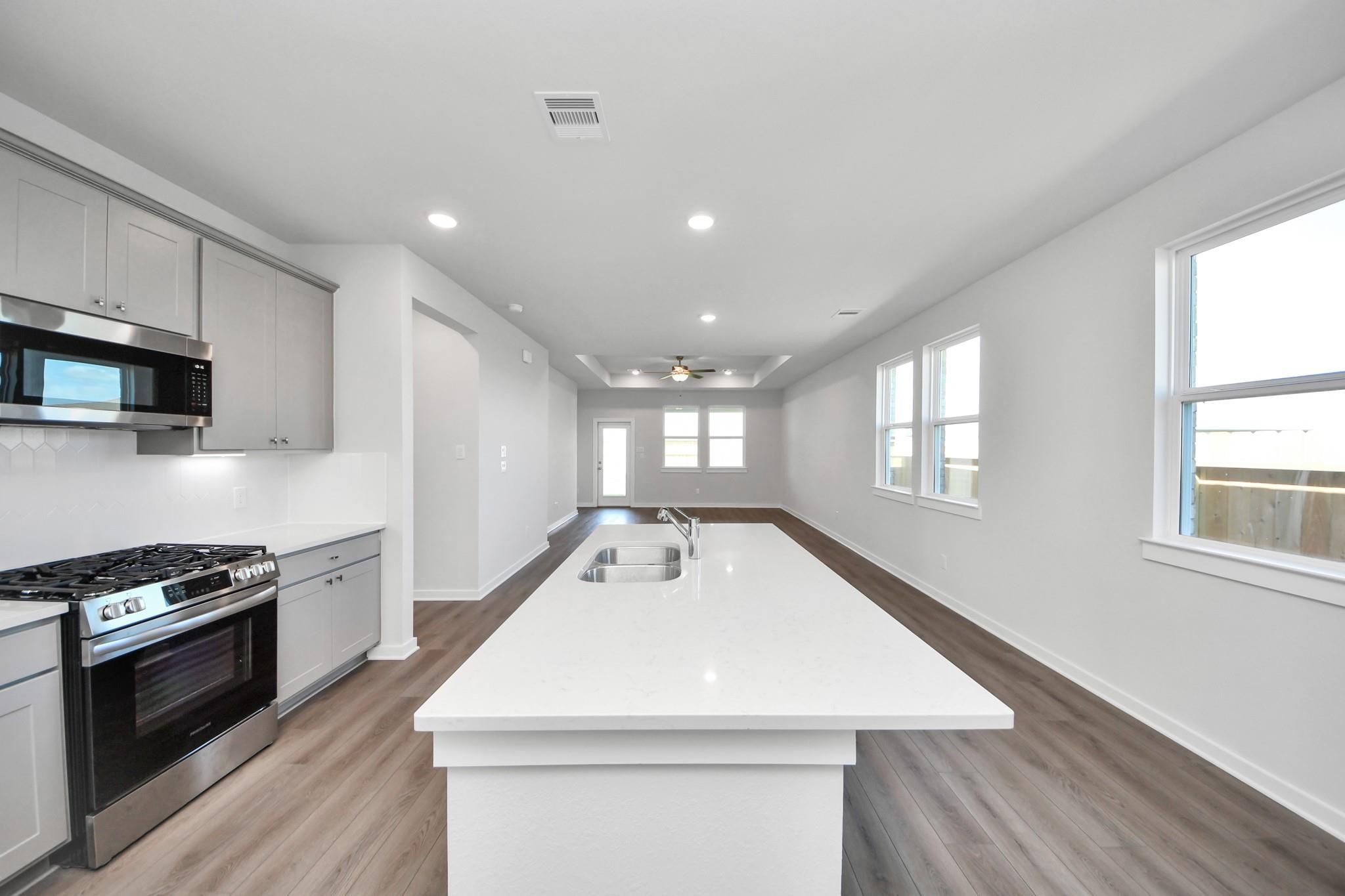 Open-concept kitchen with large island and stainless appliances in The Riviera A floor plan at Emberly in Beasley, Texas.
