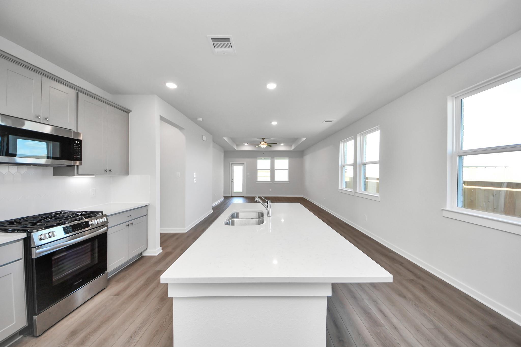Open-concept kitchen with large island and stainless appliances in The Riviera A floor plan at Emberly in Beasley, Texas.