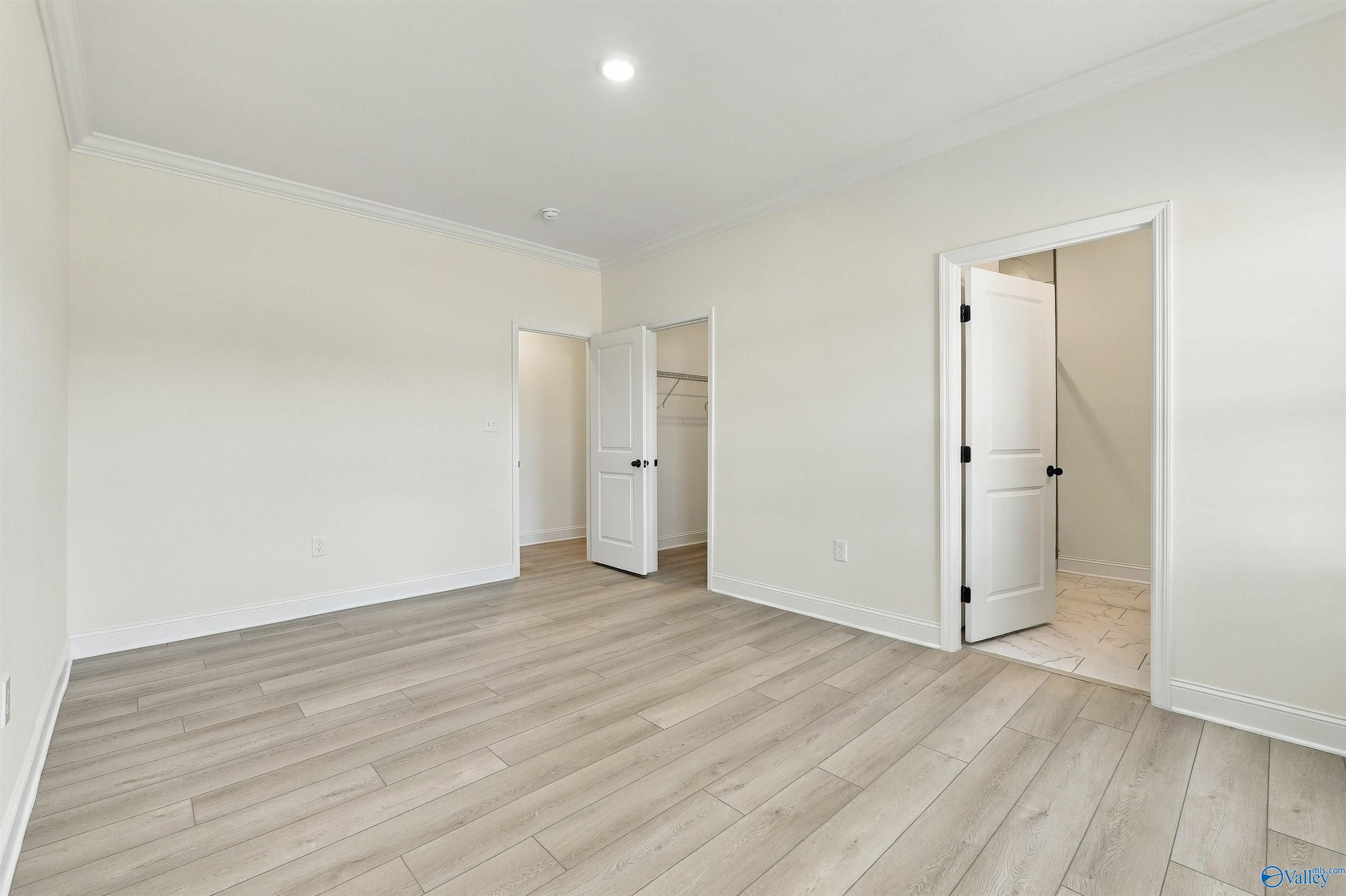 Bright bedroom with luxury vinyl plank flooring, crown molding, and open closet and bathroom doors in Davidson Homes' The Valencia, Huntsville