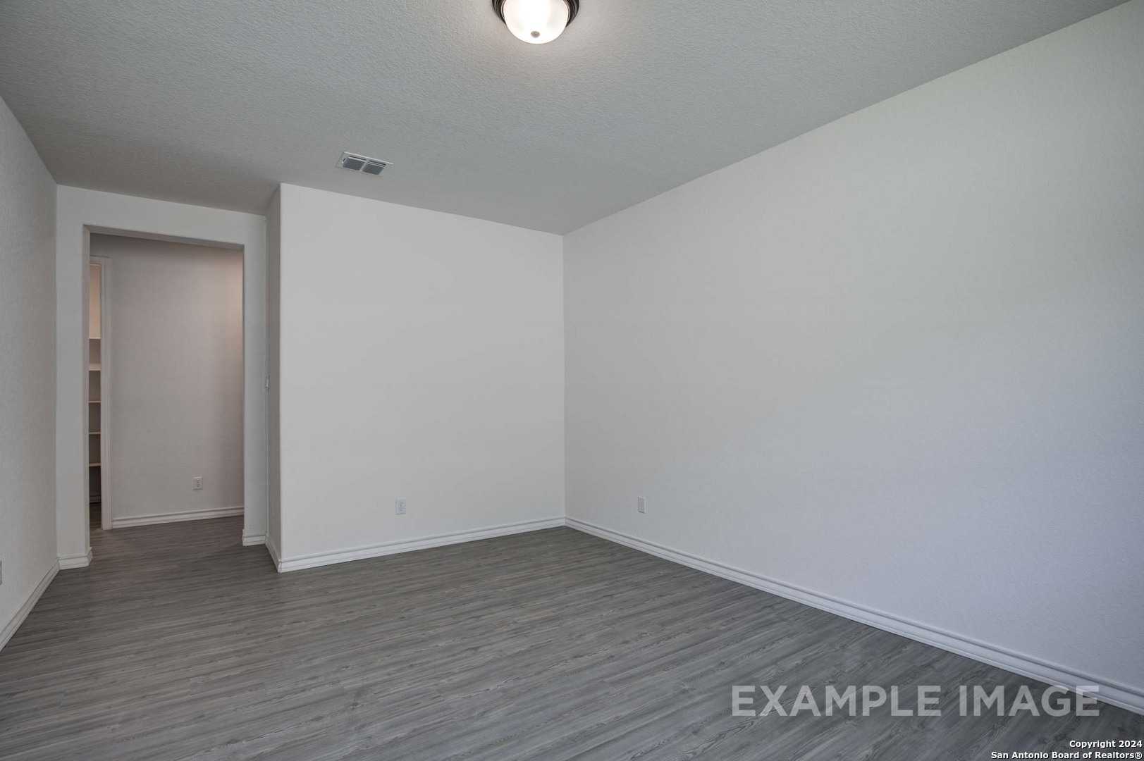 Empty bedroom with white walls, built-in closet shelves, and gray luxury vinyl flooring in Davidson Homes The Garner C, Castroville, Texas