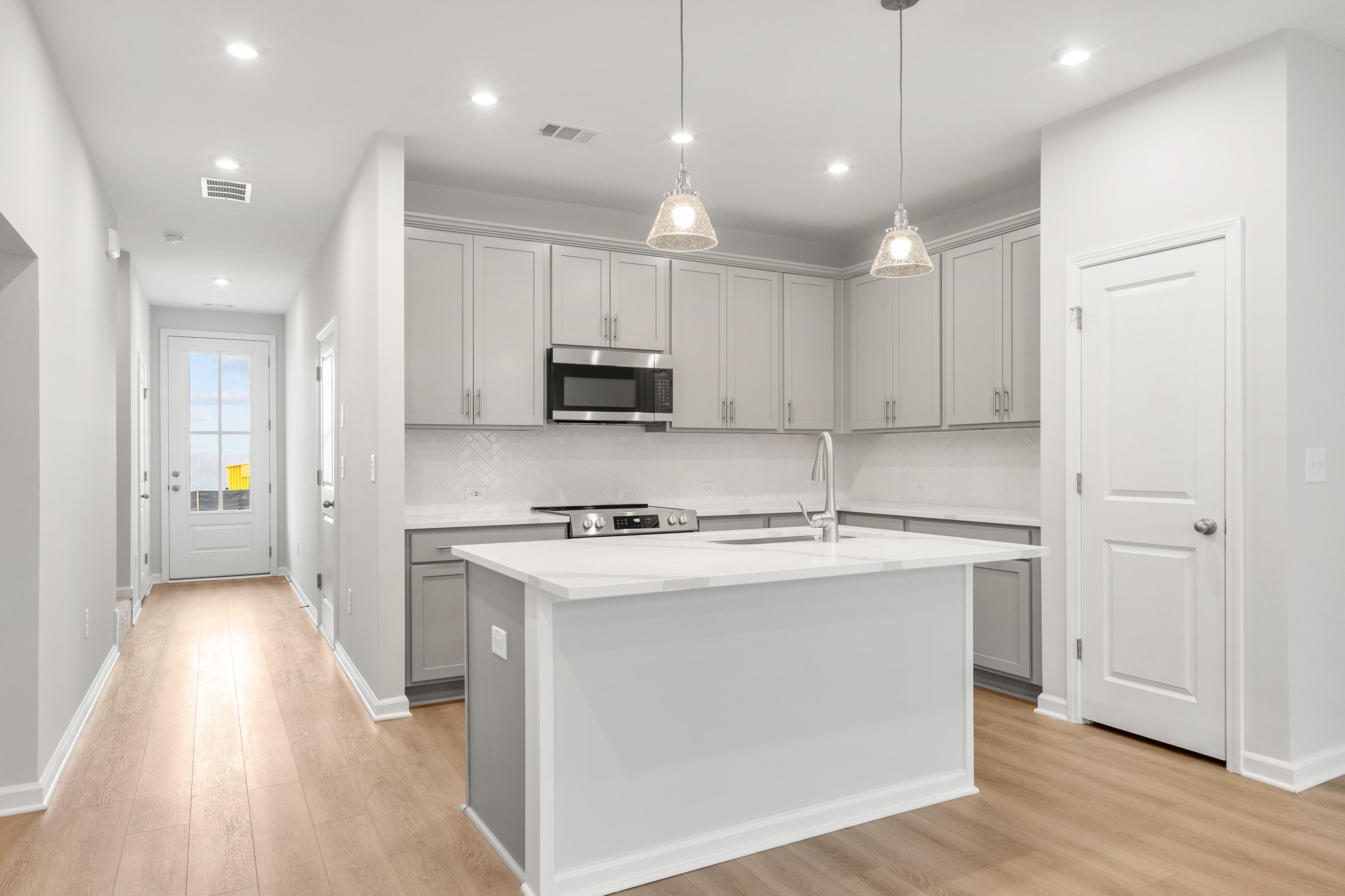 Contemporary kitchen in The Durant A with white shaker cabinets, stainless steel appliances, and large quartz island