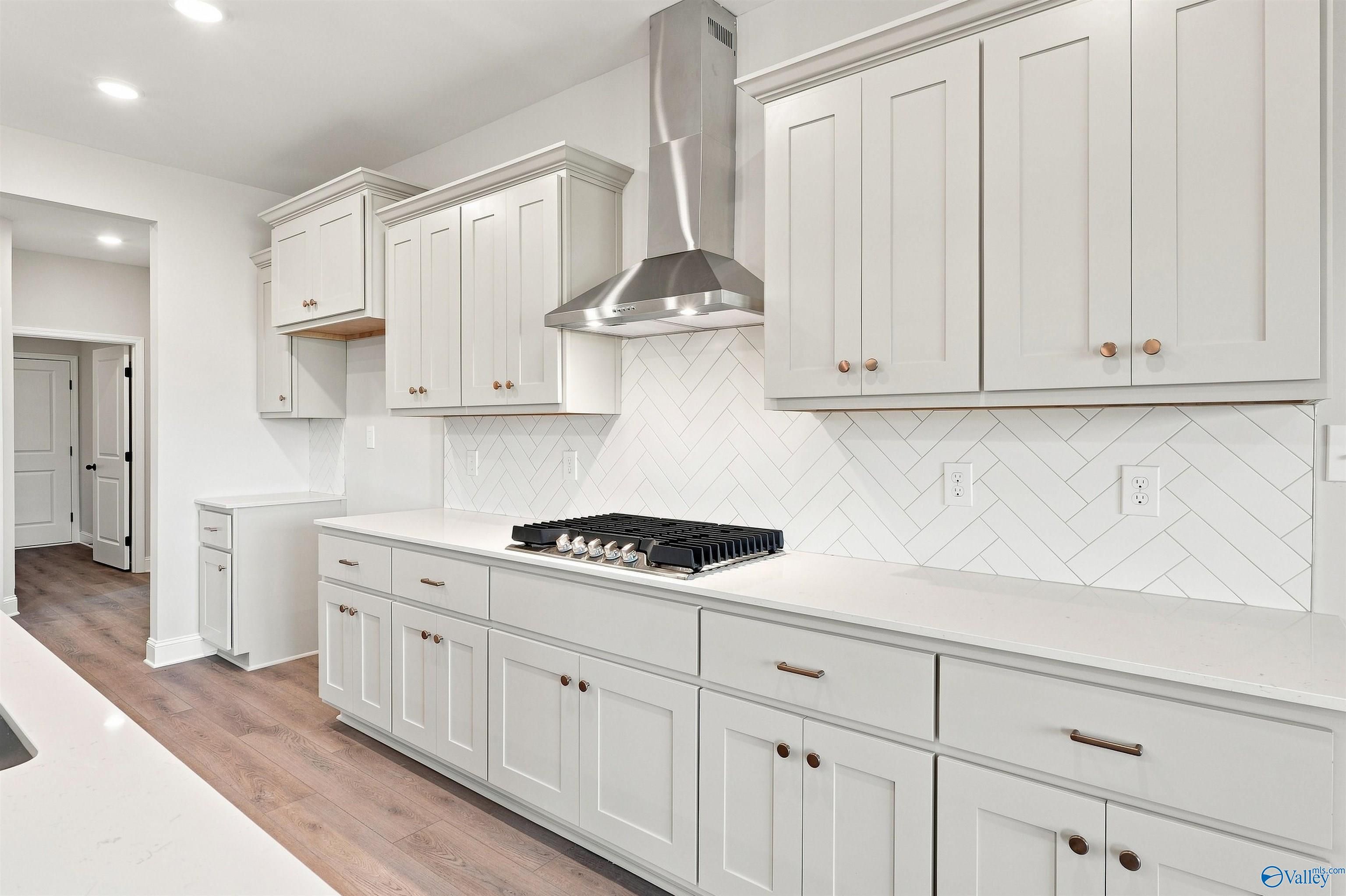 Modern kitchen with white shaker cabinets, herringbone tile backsplash, and gas cooktop in The Oxford floor plan, Toney, AL.