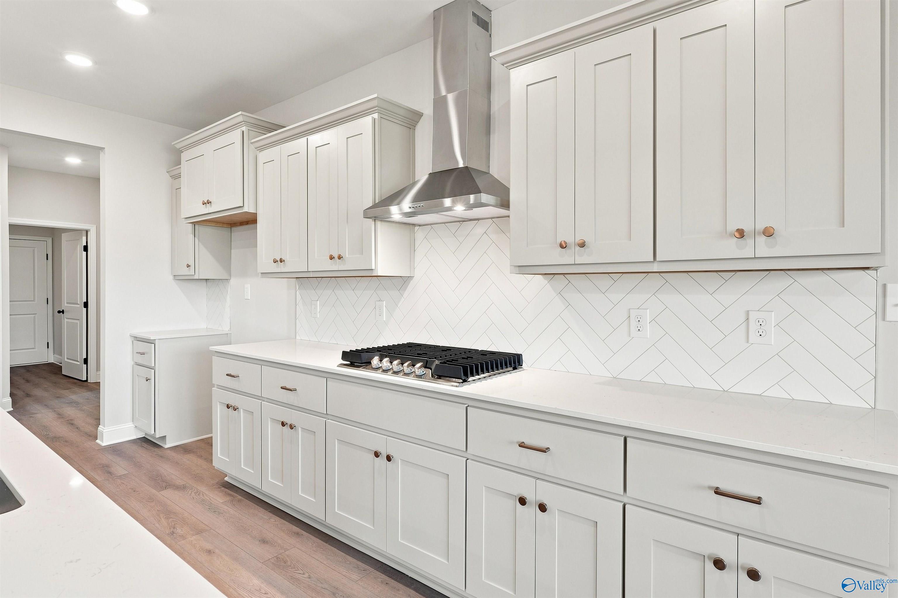 Modern kitchen with white shaker cabinets, herringbone tile backsplash, and gas cooktop in The Oxford floor plan, Toney, AL.