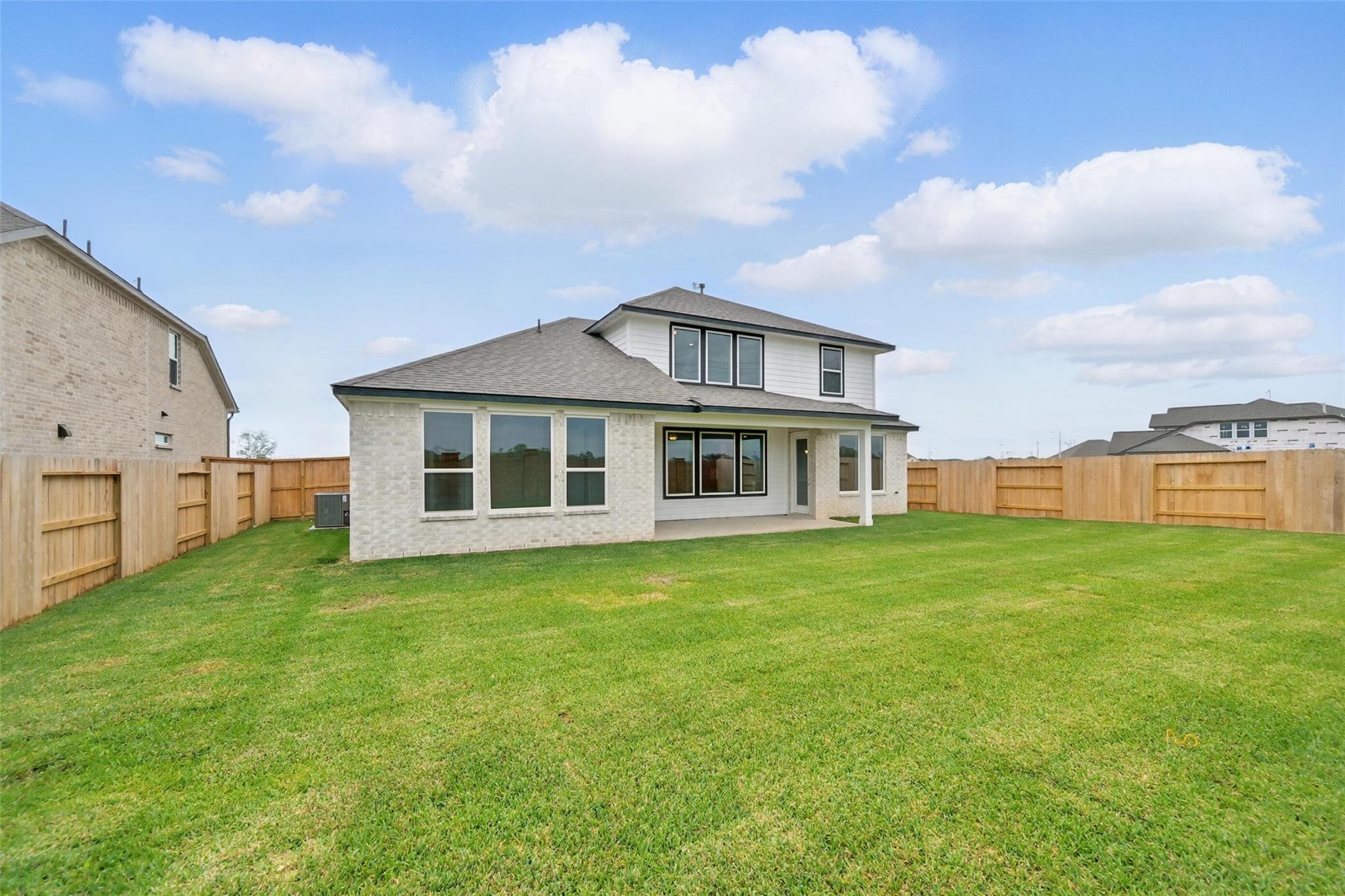 Rear view of two-story Philip A home featuring covered patio, large windows, and fenced lush backyard in Lago Mar, Texas City