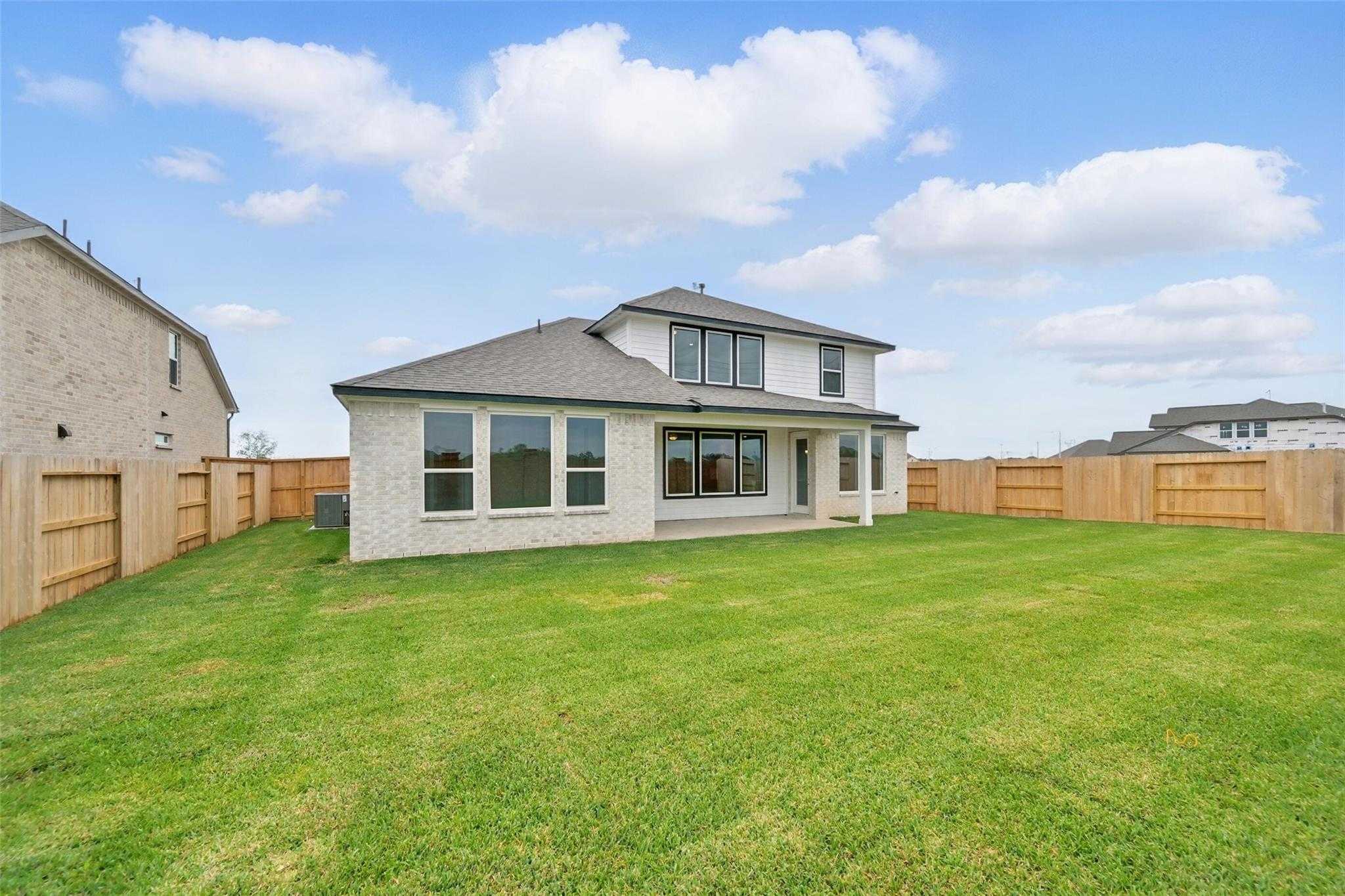 Rear view of two-story Philip A home featuring covered patio, large windows, and fenced lush backyard in Lago Mar, Texas City