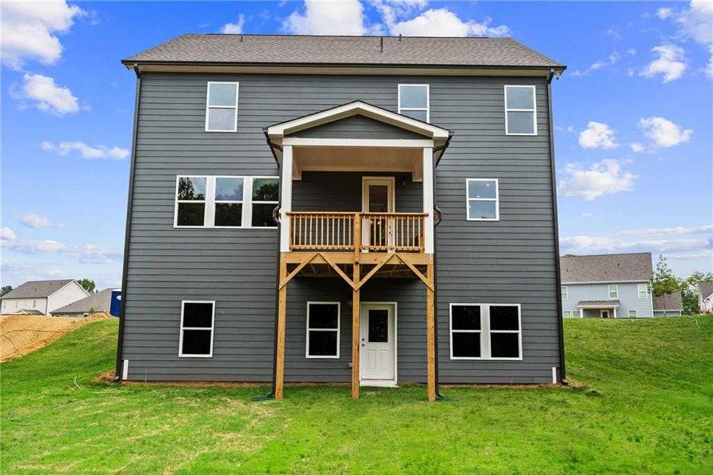 Three-story gray Hickory B home rear view with upper wooden deck, large windows, and green backyard in Wehunt Meadows, Hoschton, GA
