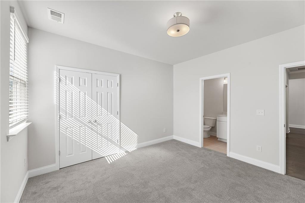 Bright bedroom with gray carpet, white double-door closet, and en-suite bath in Davidson Homes The Harrison G, Cedar Farms, Winder GA