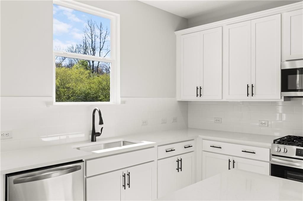 Modern white kitchen featuring stainless appliances, quartz counters, and garden-view window in Davidson Homes The Hickory B, Winder, GA