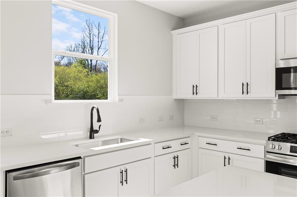 Modern white kitchen featuring stainless appliances, quartz counters, and garden-view window in Davidson Homes The Hickory B, Winder, GA