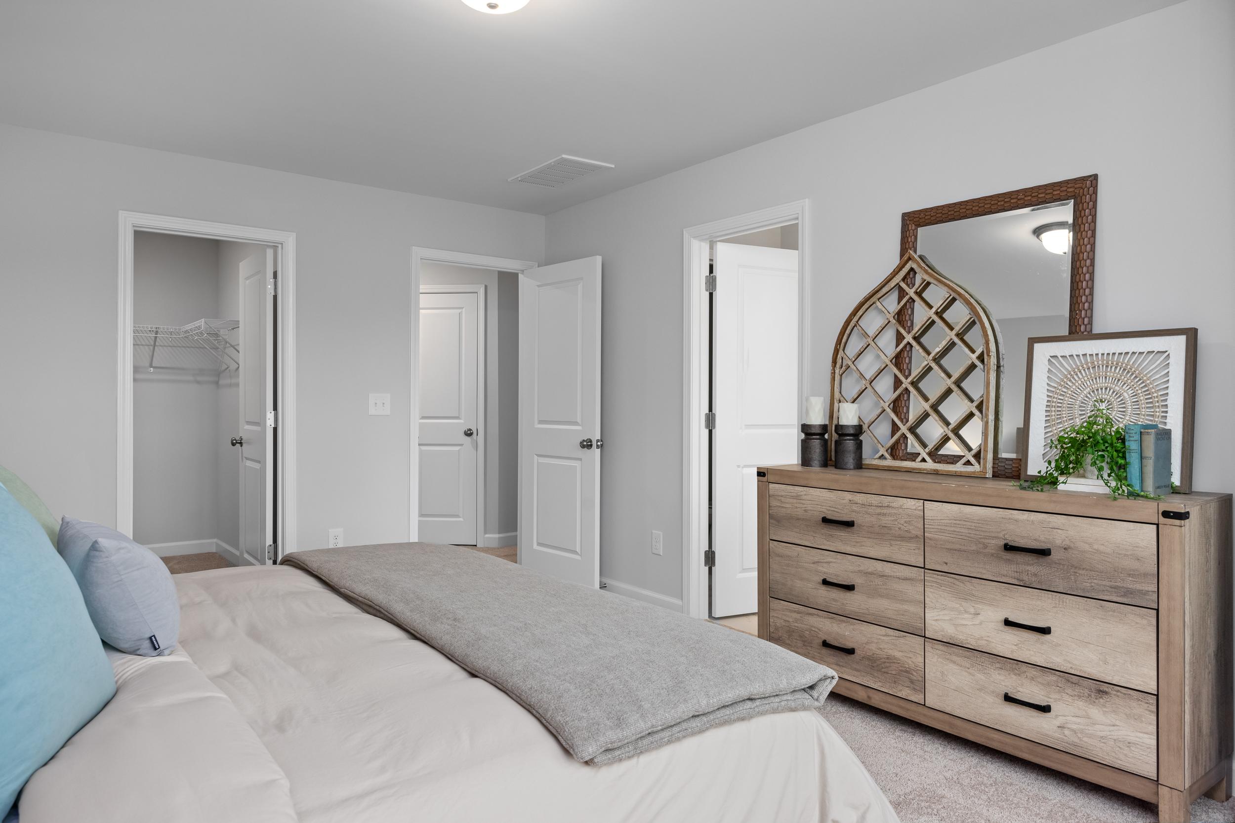 Spacious master suite bedroom in The Warren featuring a dresser, walk-in closet, and neutral decor in Lillington, NC.