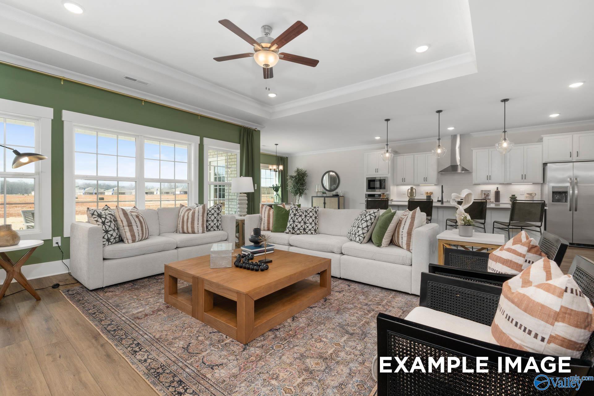 Spacious open-concept living room with white sectional sofa, wooden coffee table, ceiling fan, and adjacent modern kitchen in The Finleigh home, Decatur, Alabama