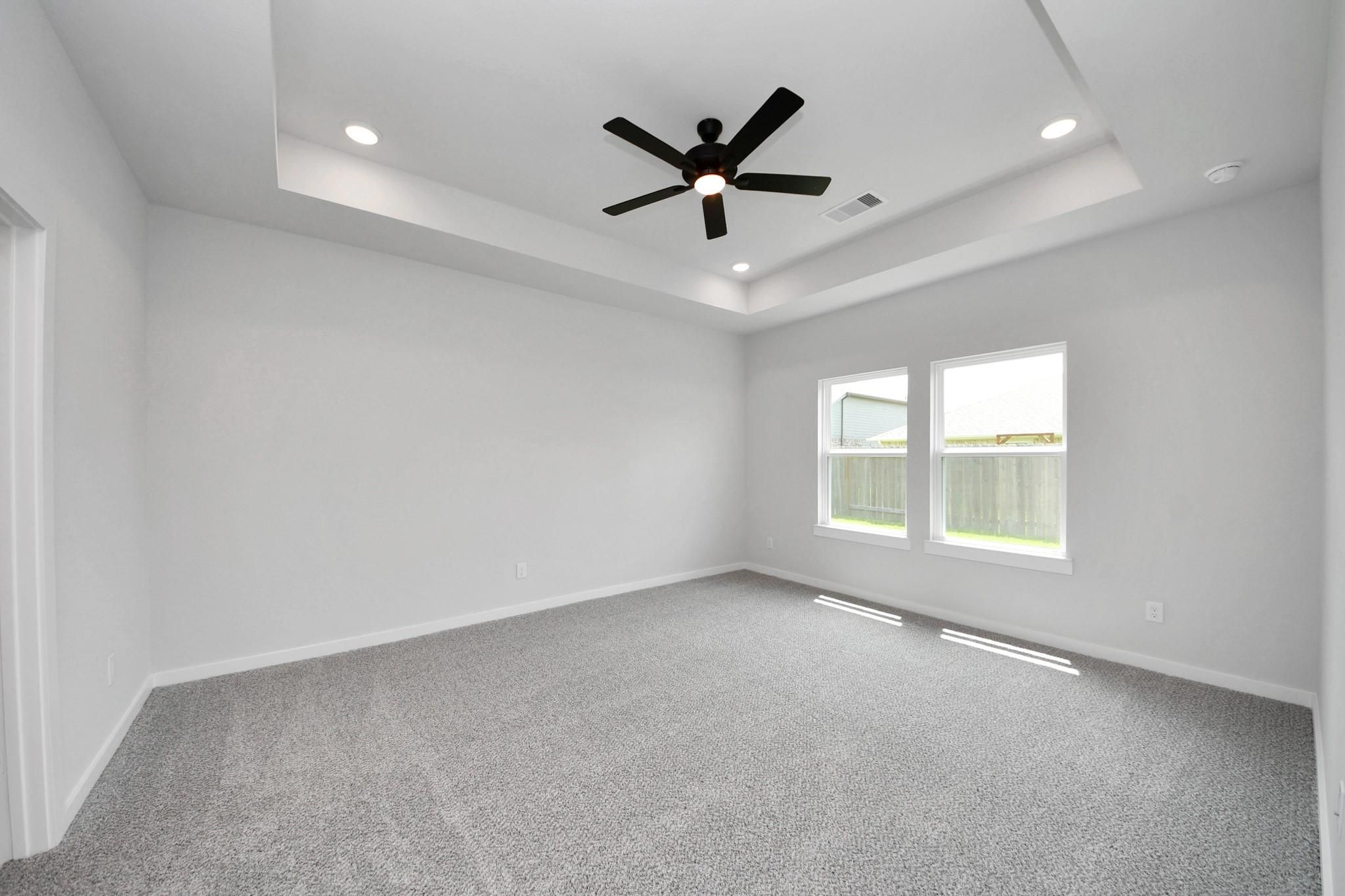 Spacious bedroom with tray ceiling and ceiling fan in The Everett C floor plan at River Ranch Meadows in Dayton, Texas.