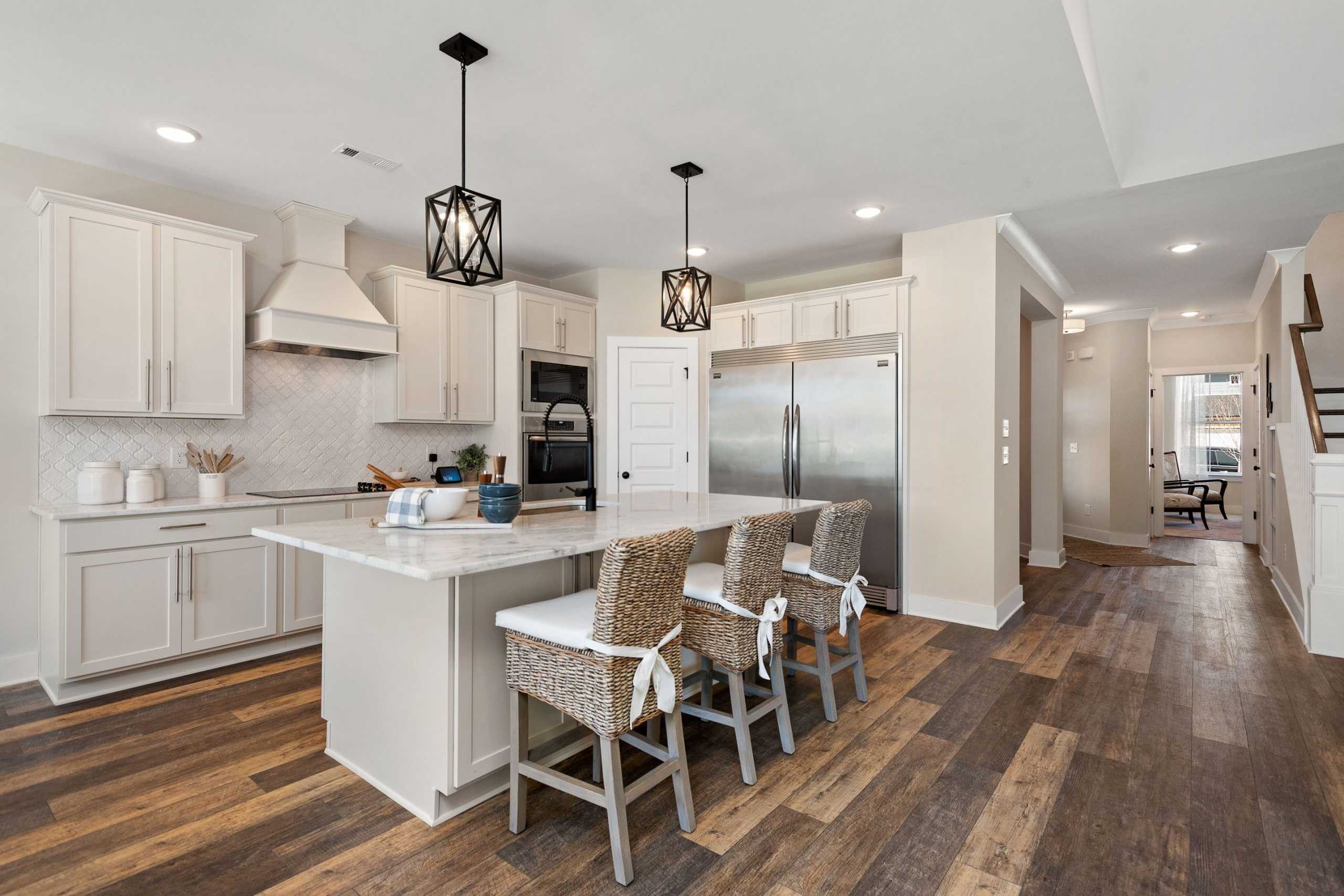 Spacious modern kitchen at Rivers Edge in Murfreesboro TN with white cabinets, quartz island, woven bar stools, and hardwood floors