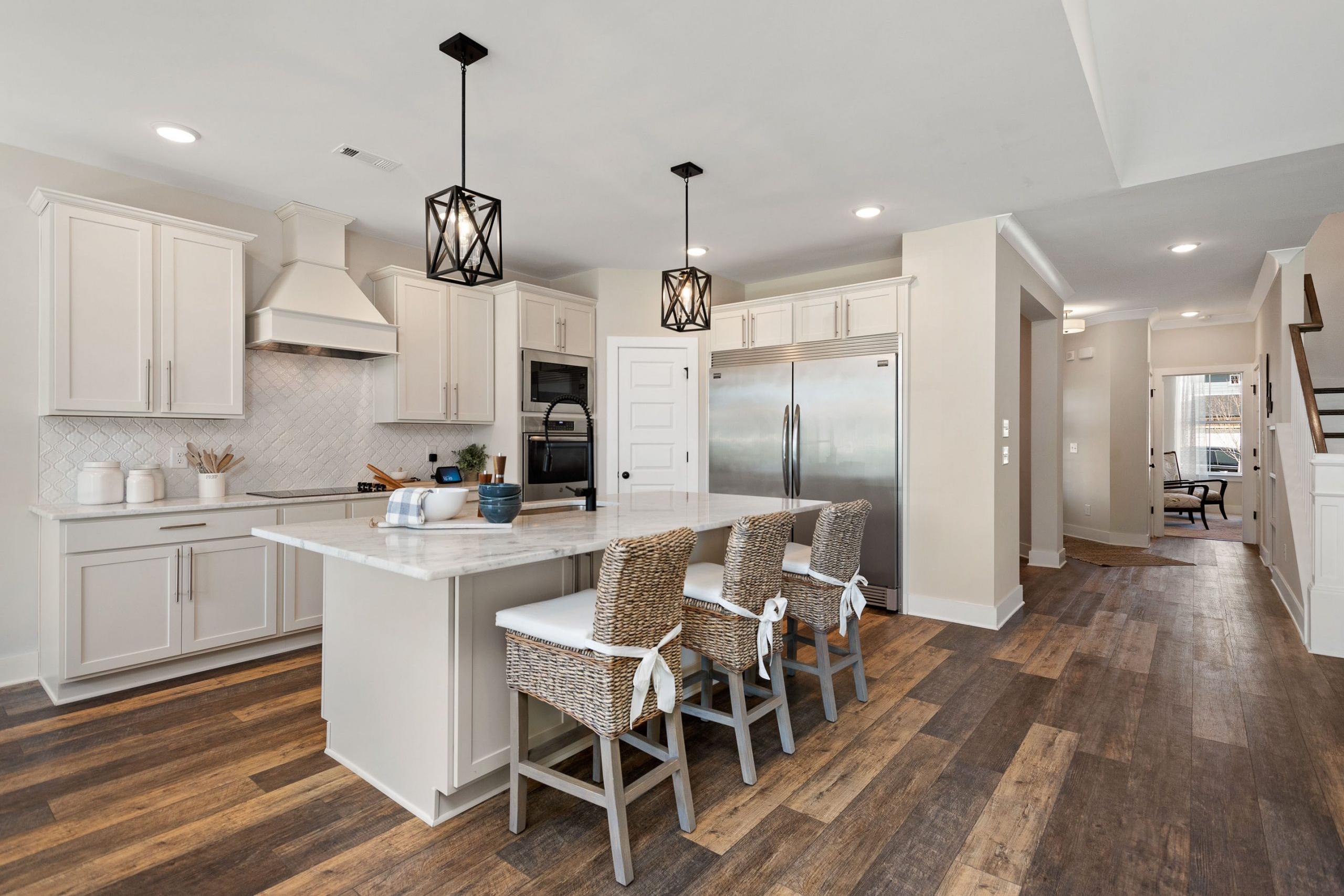 Spacious modern kitchen at Rivers Edge in Murfreesboro TN with white cabinets, quartz island, woven bar stools, and hardwood floors
