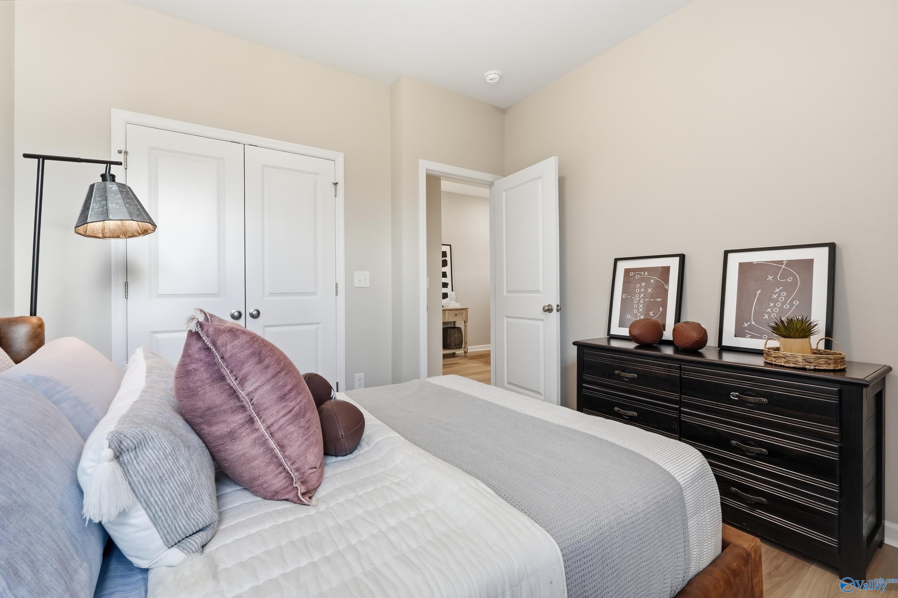 Cozy bedroom with gray bedding, purple pillows, black dresser, and abstract art in Davidson Homes The Polaris, Fayetteville, TN