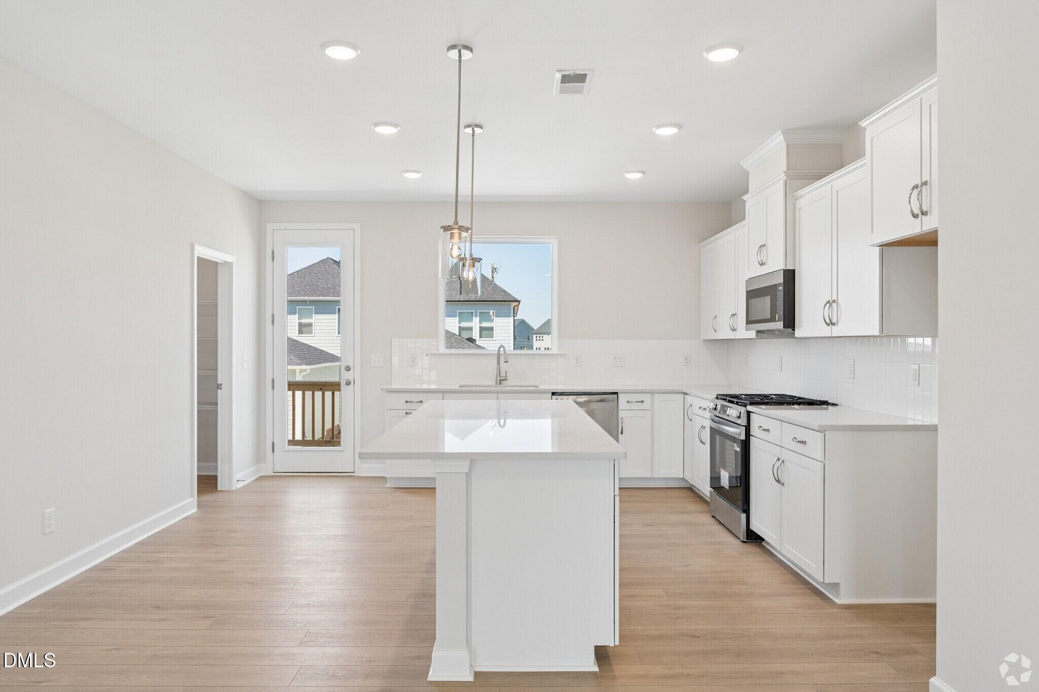 Bright white kitchen with large island, pendant lights, stainless appliances, and hardwood floors in Davidson Homes' The Avery, Knightdale NC