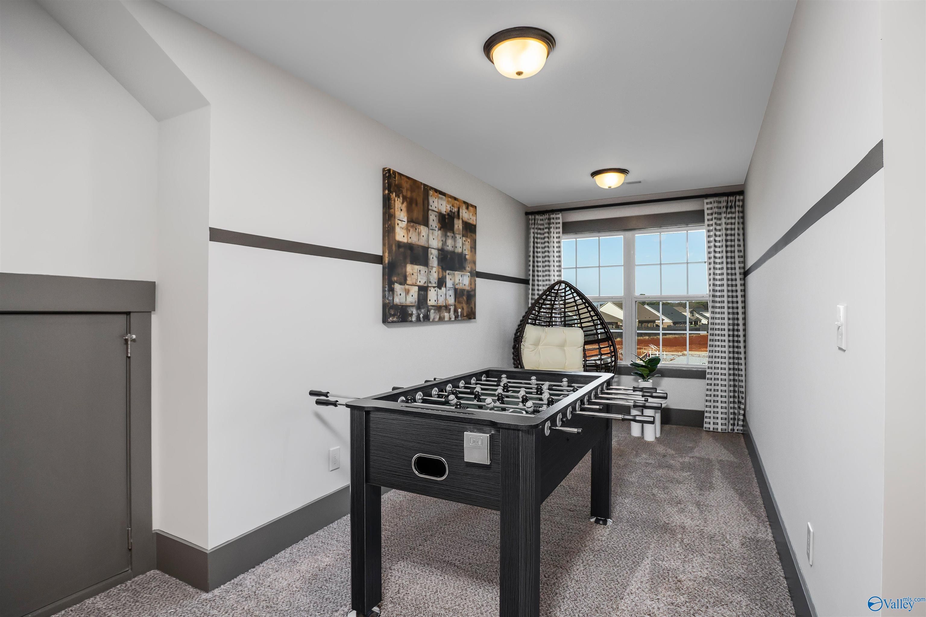 Cozy bonus game room featuring black foosball table, rattan hanging chair, and abstract wall art in Davidson Homes The Rockford B with Bonus, Madison, Alabama