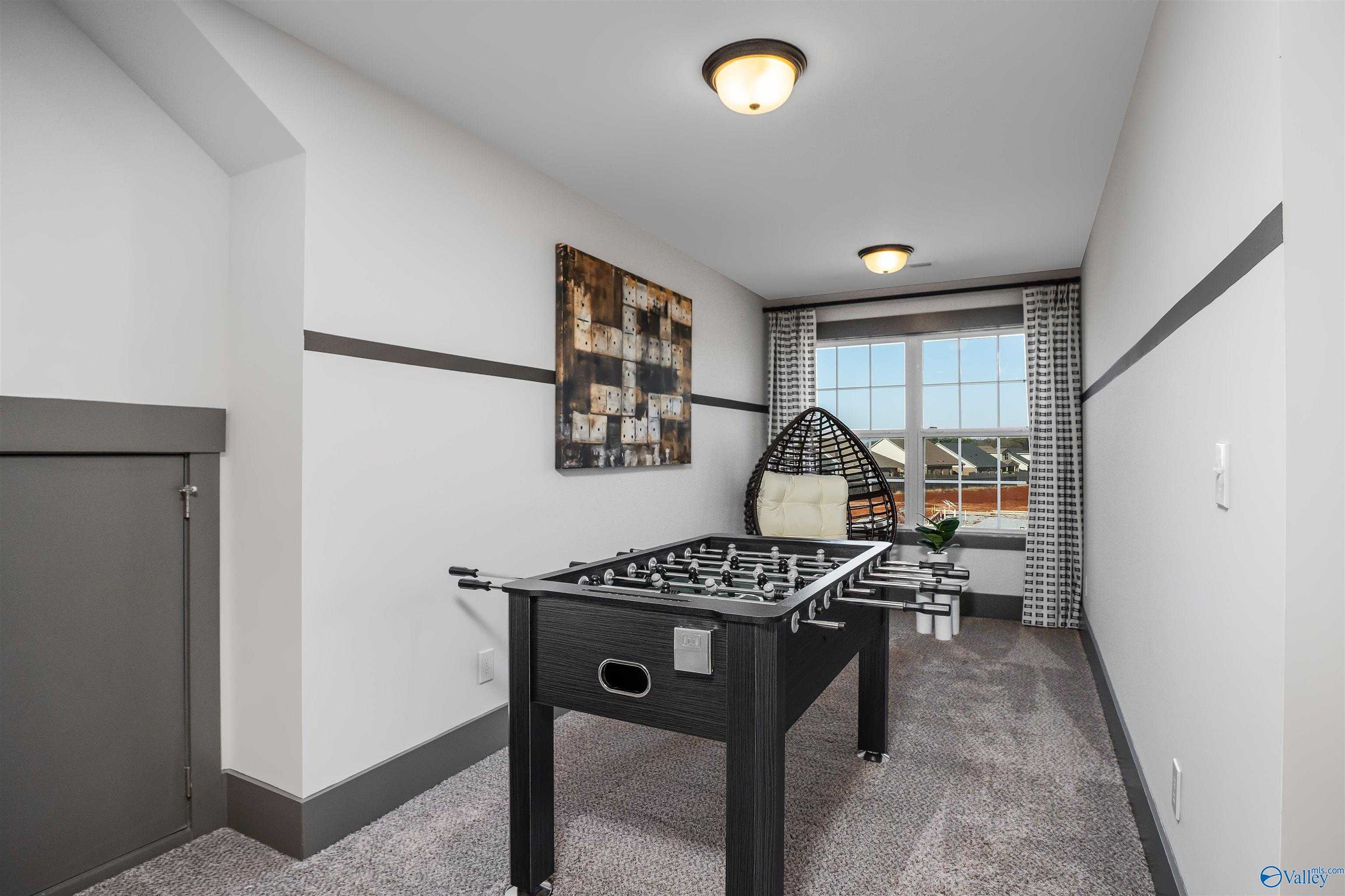 Cozy bonus game room featuring black foosball table, rattan hanging chair, and abstract wall art in Davidson Homes The Rockford B with Bonus, Madison, Alabama