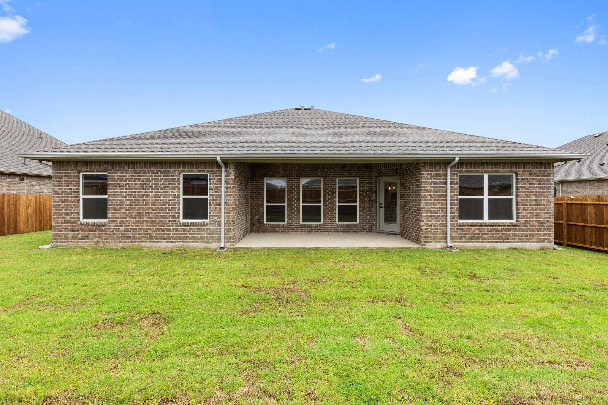Rear elevation of The Harrison single-story home with brick facade, covered patio, large windows, and lush green backyard in Josephine, Texas