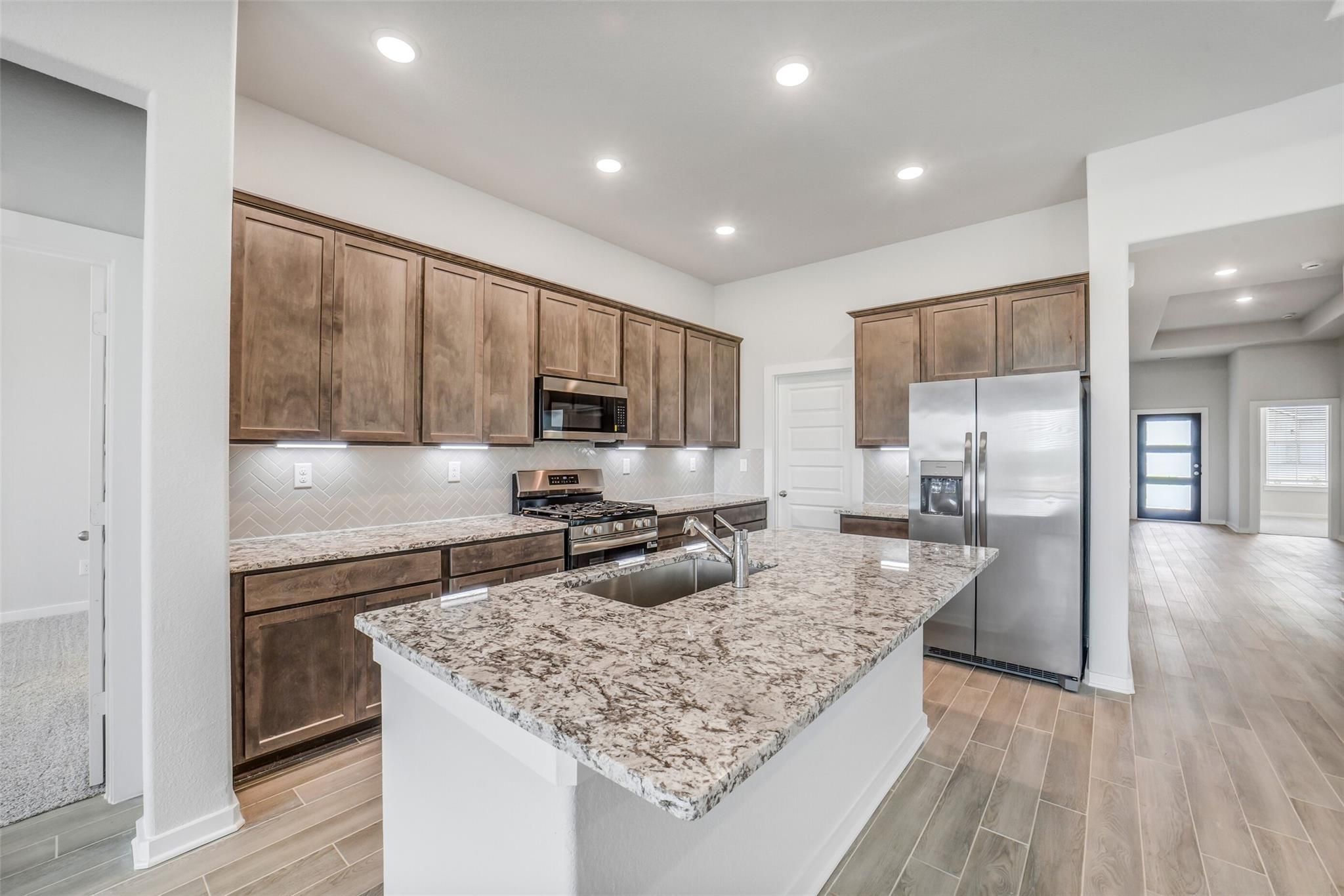Modern kitchen featuring granite island, stainless steel appliances, shaker cabinets in Davidson Homes The Acadia C, Magnolia TX