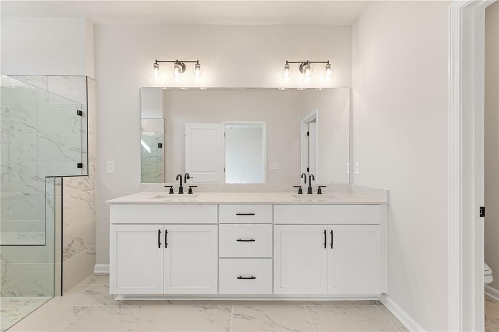 Elegant master bathroom with double white vanity, quartz counters, frameless glass shower in Davidson Homes The Glenwood C, Loganville, GA