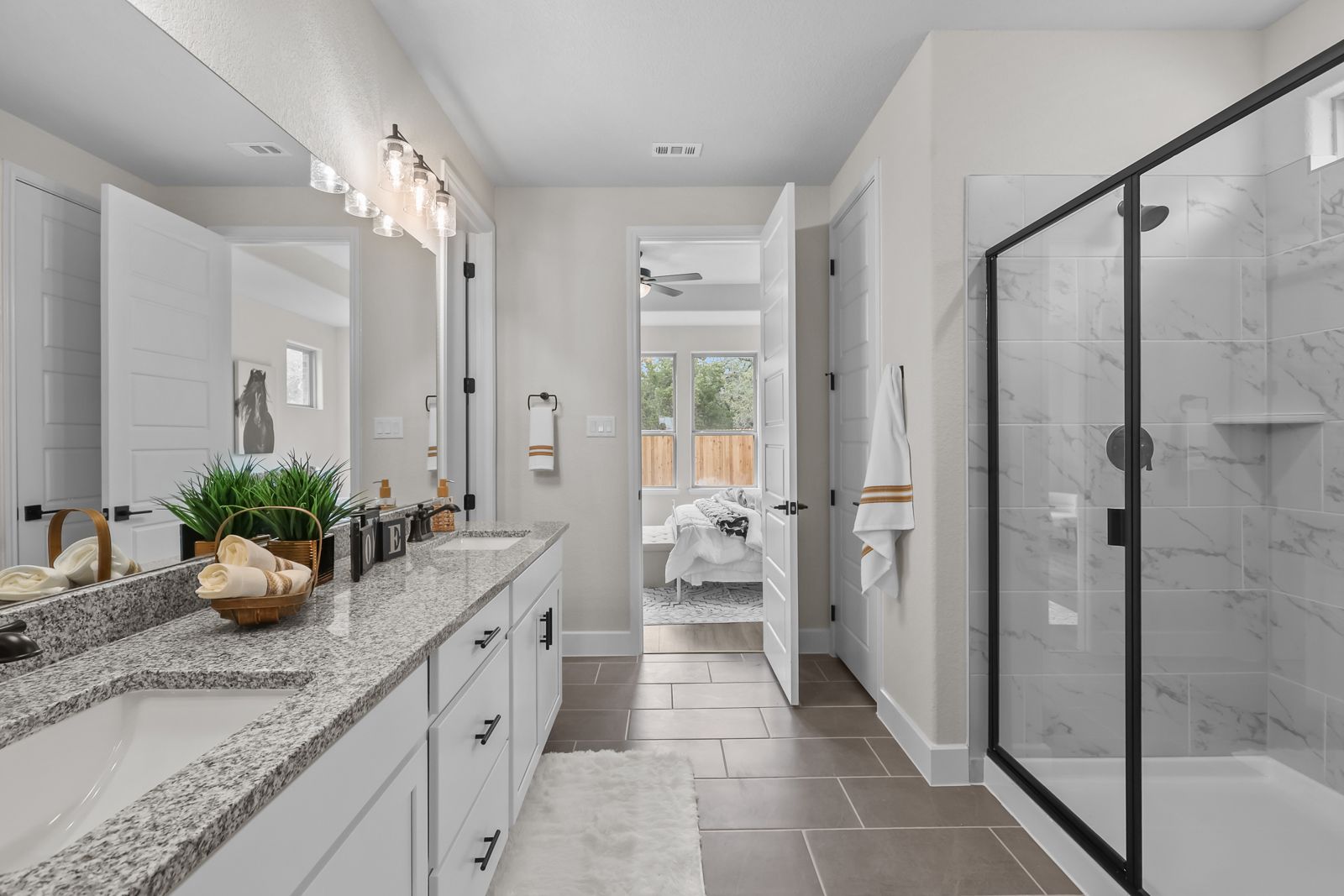 Master bathroom in The Belmont J featuring dual vanity, granite countertops, and walk-in shower with black frame accents.