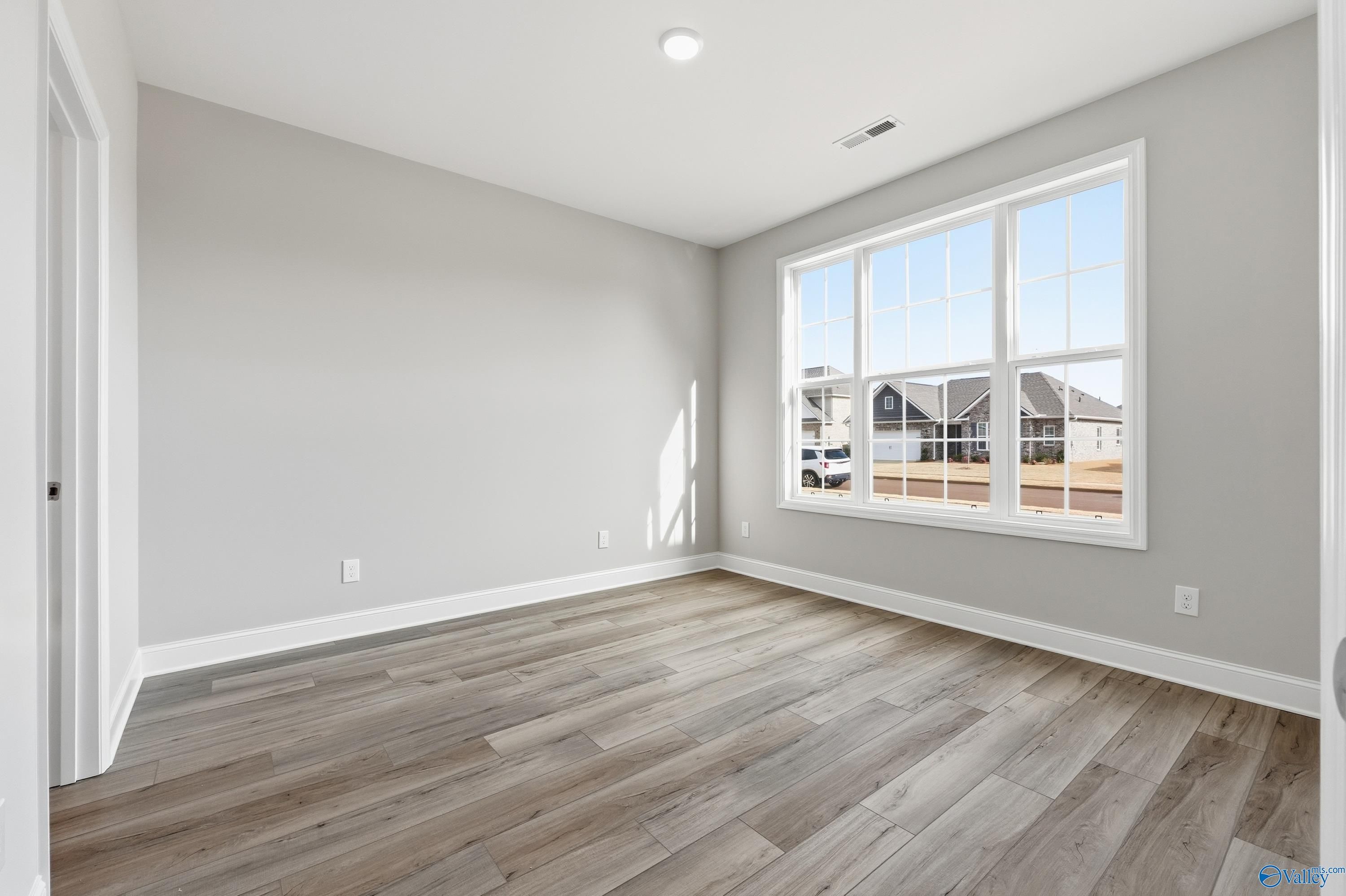 Bright bedroom with large triple window overlooking neighborhood, gray walls, and luxury vinyl plank flooring in The Lanier, Meridianville, Alabama