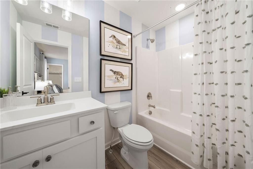 Bright bathroom with blue striped walls, bird artwork, white tub shower, vanity sink in Davidson Homes Willow B, Dallas, Georgia