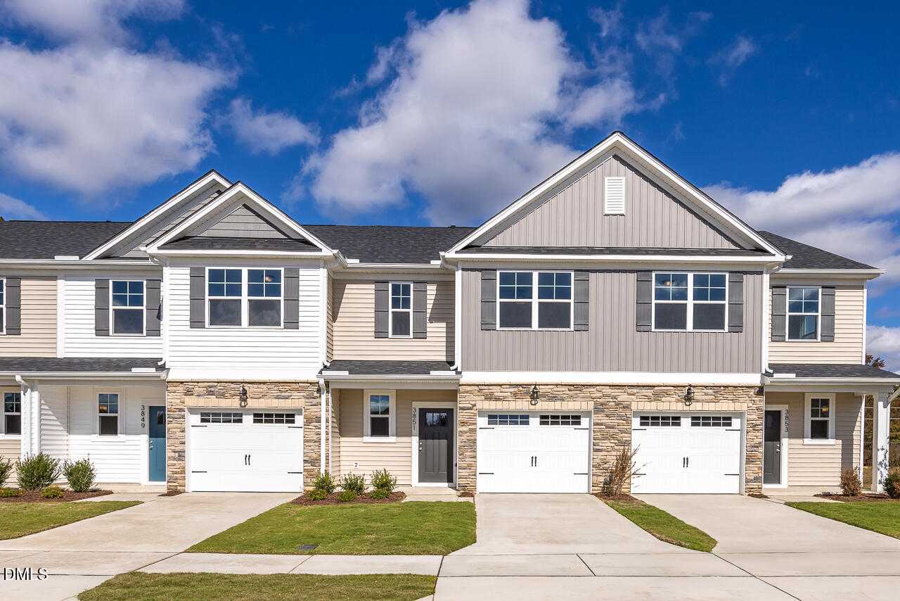 Modern two-story townhomes with beige siding, brick bases, 1-car garages, and front porches in Springvale, Fuquay-Varina, NC