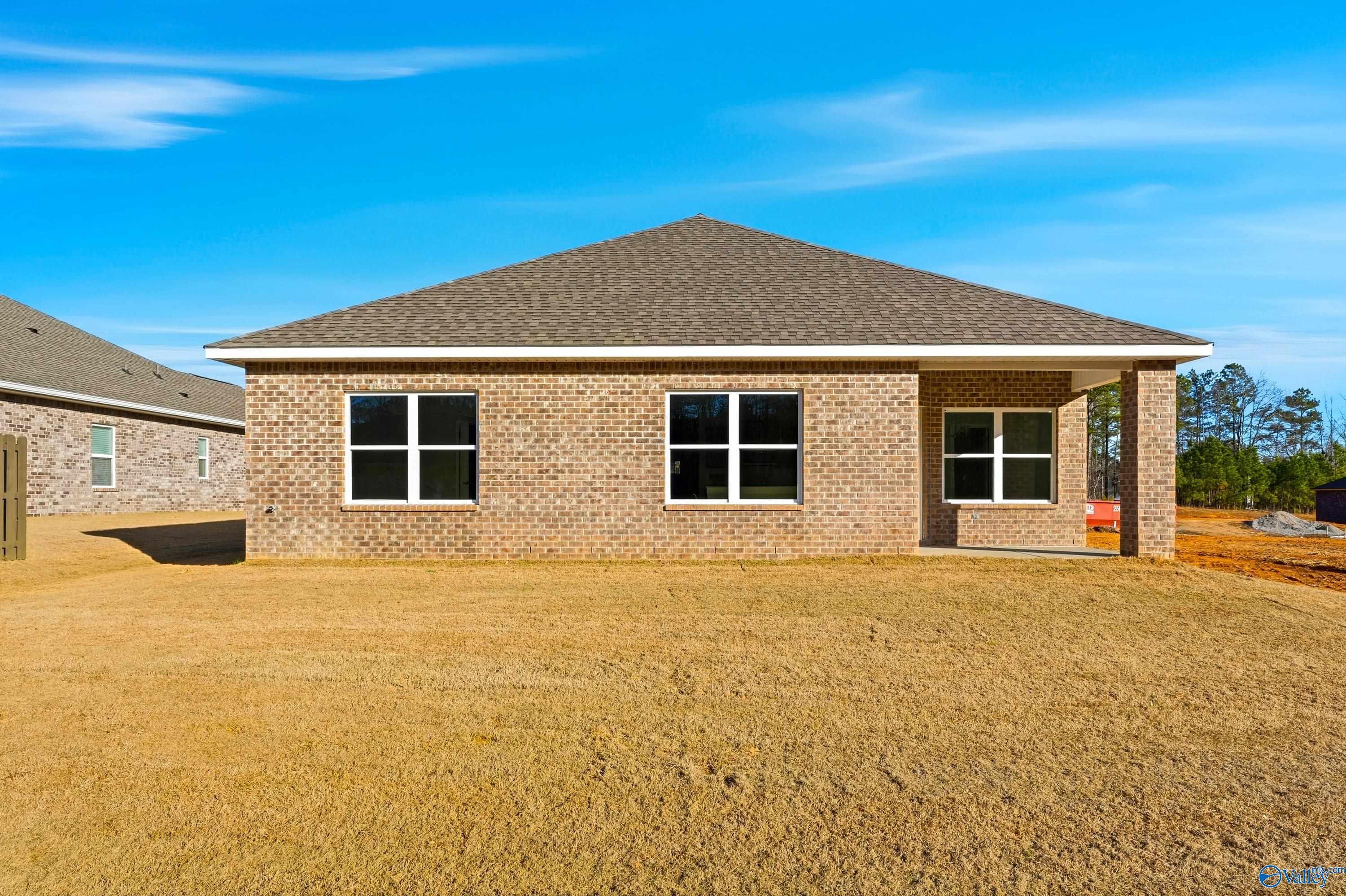 Tan brick 1-story home with gabled roof, large windows, covered porch, and grassy yard in The Highlands, Arab, Alabama by Davidson Homes