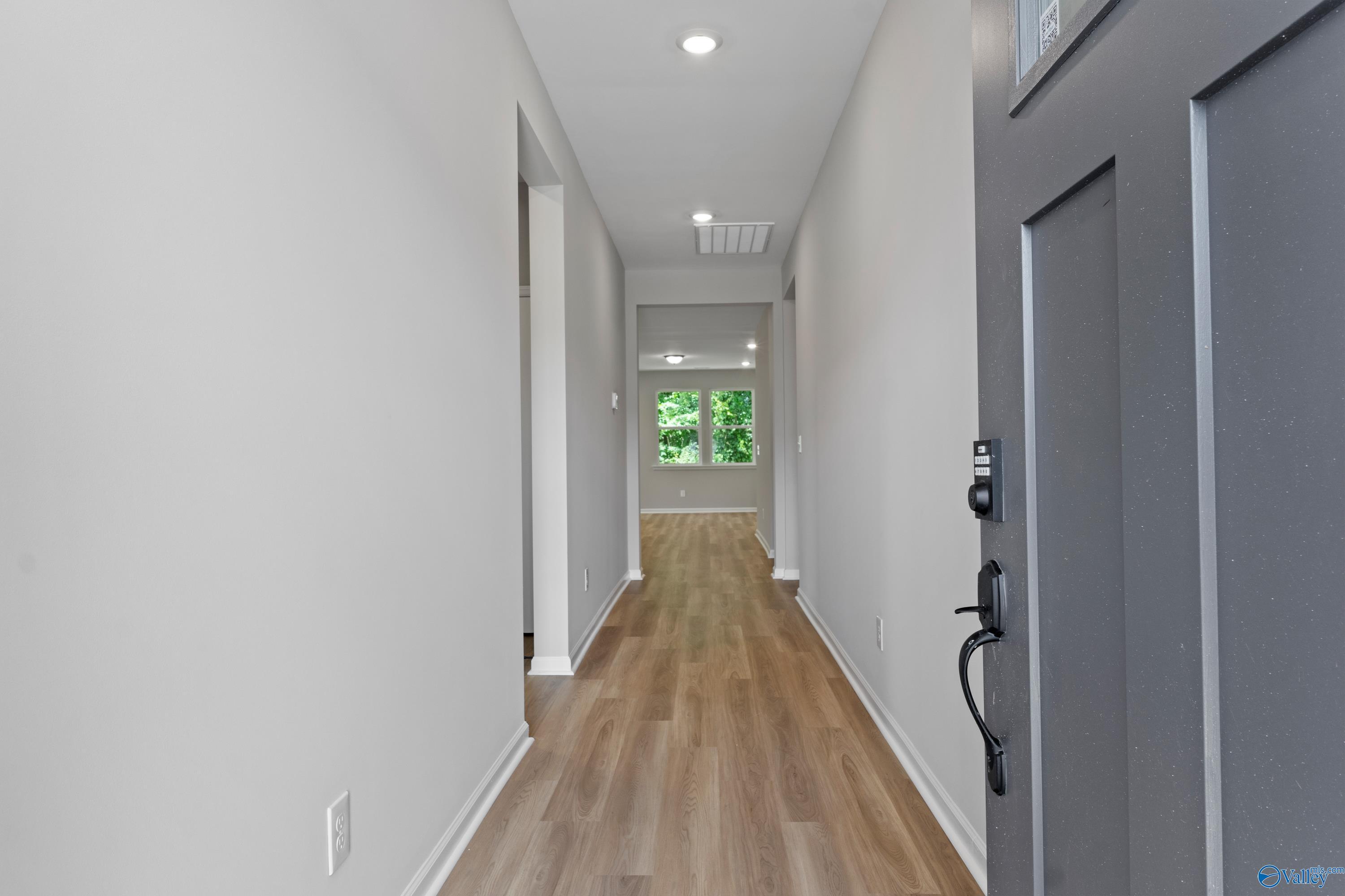 Bright hallway with light gray walls, hardwood floors, and window views in Davidson Homes The Phoenix, Hazel Green, Alabama