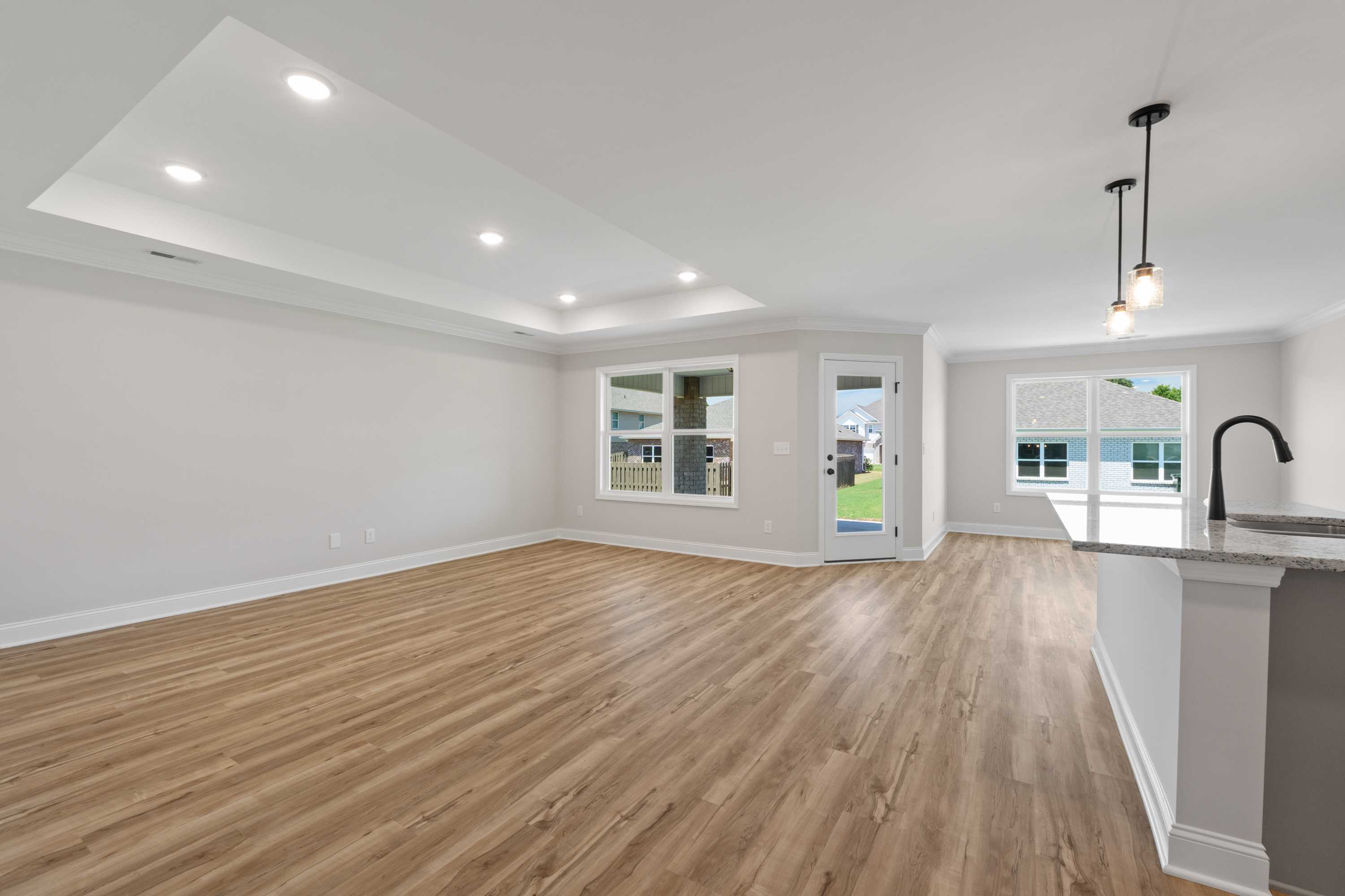 Spacious open-concept living room and kitchen in The Everett C with hardwood floors, white cabinets, and large windows
