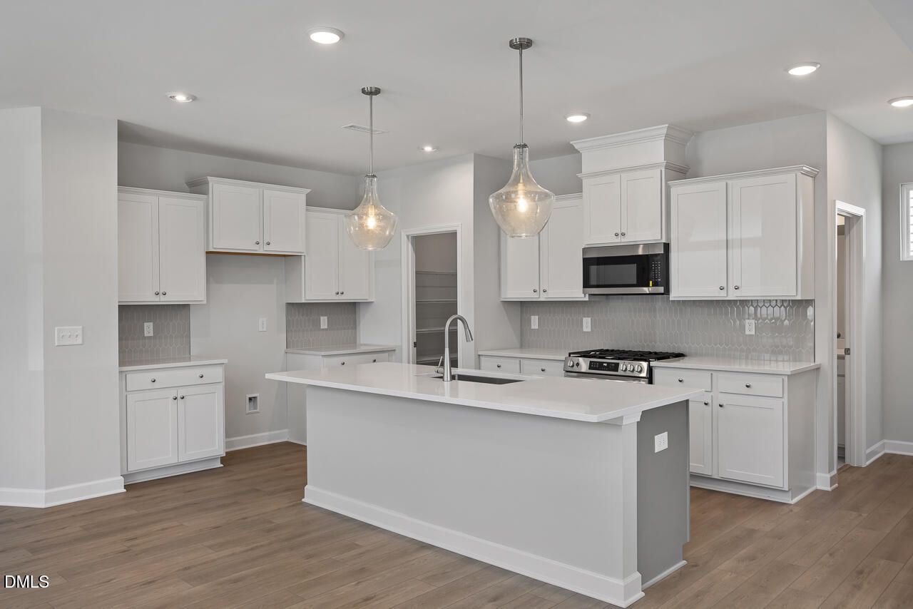 Modern white kitchen with quartz island and pendant lighting in The Adalynn B floor plan at Gregory Village, Lillington.