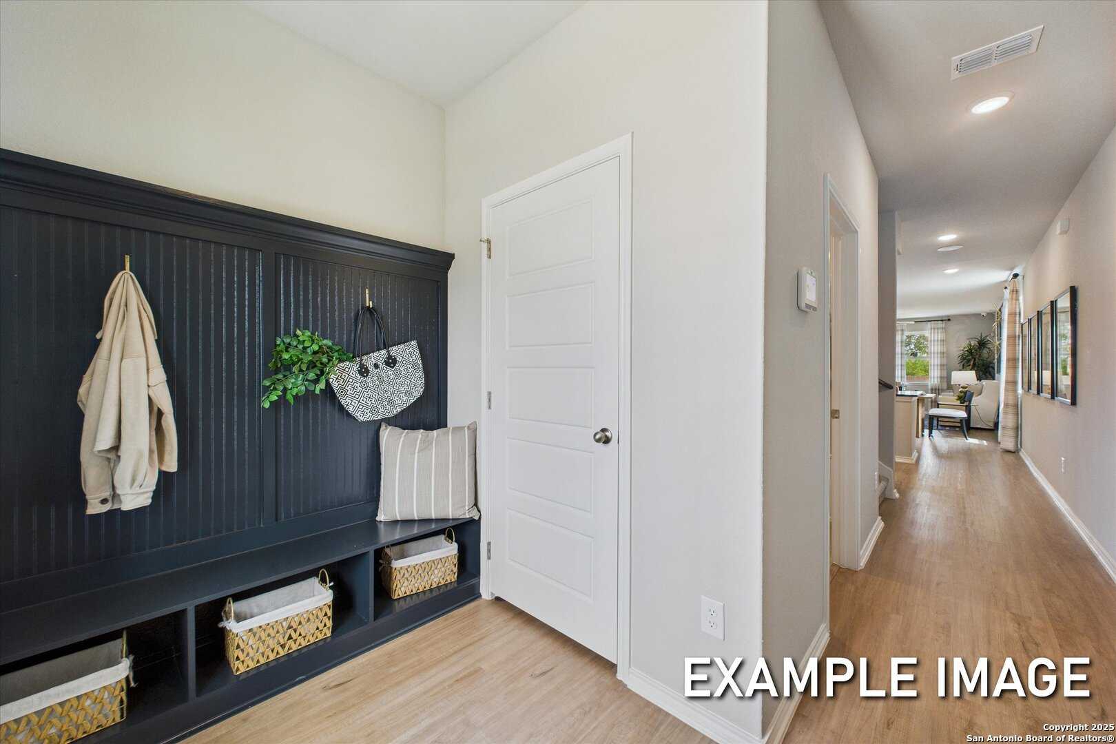 Cozy mudroom with dark wood bench, coat hooks, wicker baskets, and hallway view in Davidson Homes The Sabine C, San Antonio