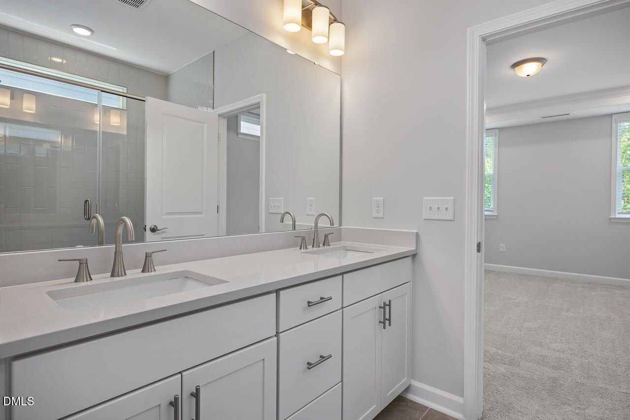 Double vanity bathroom with white cabinets and glass shower in The Ashport L floor plan, Sage on North Main, Wake Forest, NC