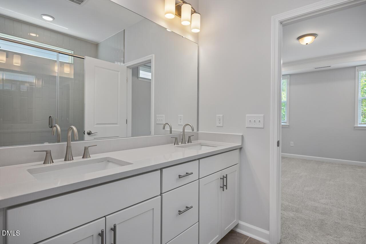 Double vanity bathroom with white cabinets and glass shower in The Ashport L floor plan, Sage on North Main, Wake Forest, NC