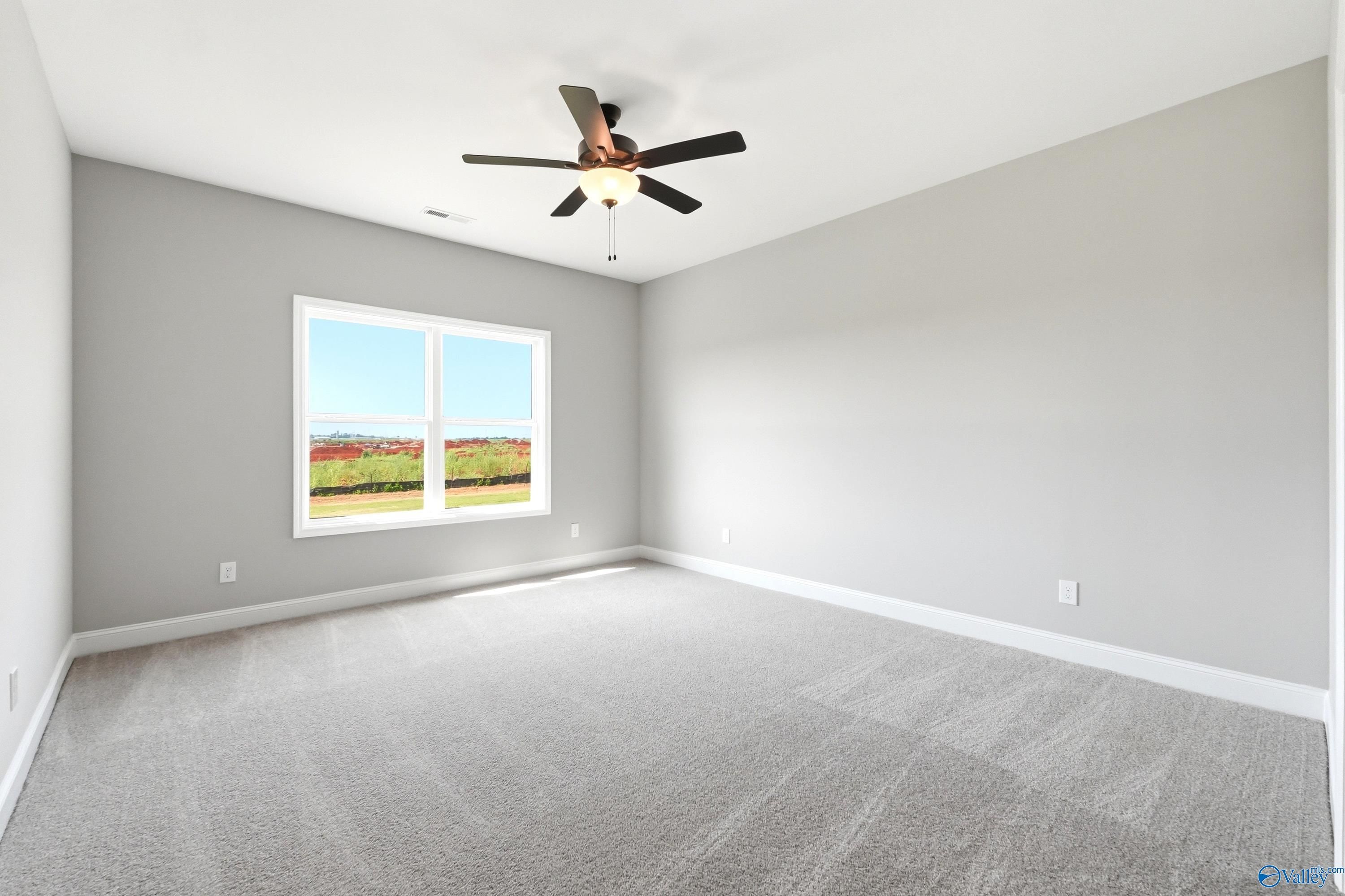 Spacious bedroom with grey carpet and ceiling fan in The Daphne D floor plan at Creekside in Harvest, Alabama.