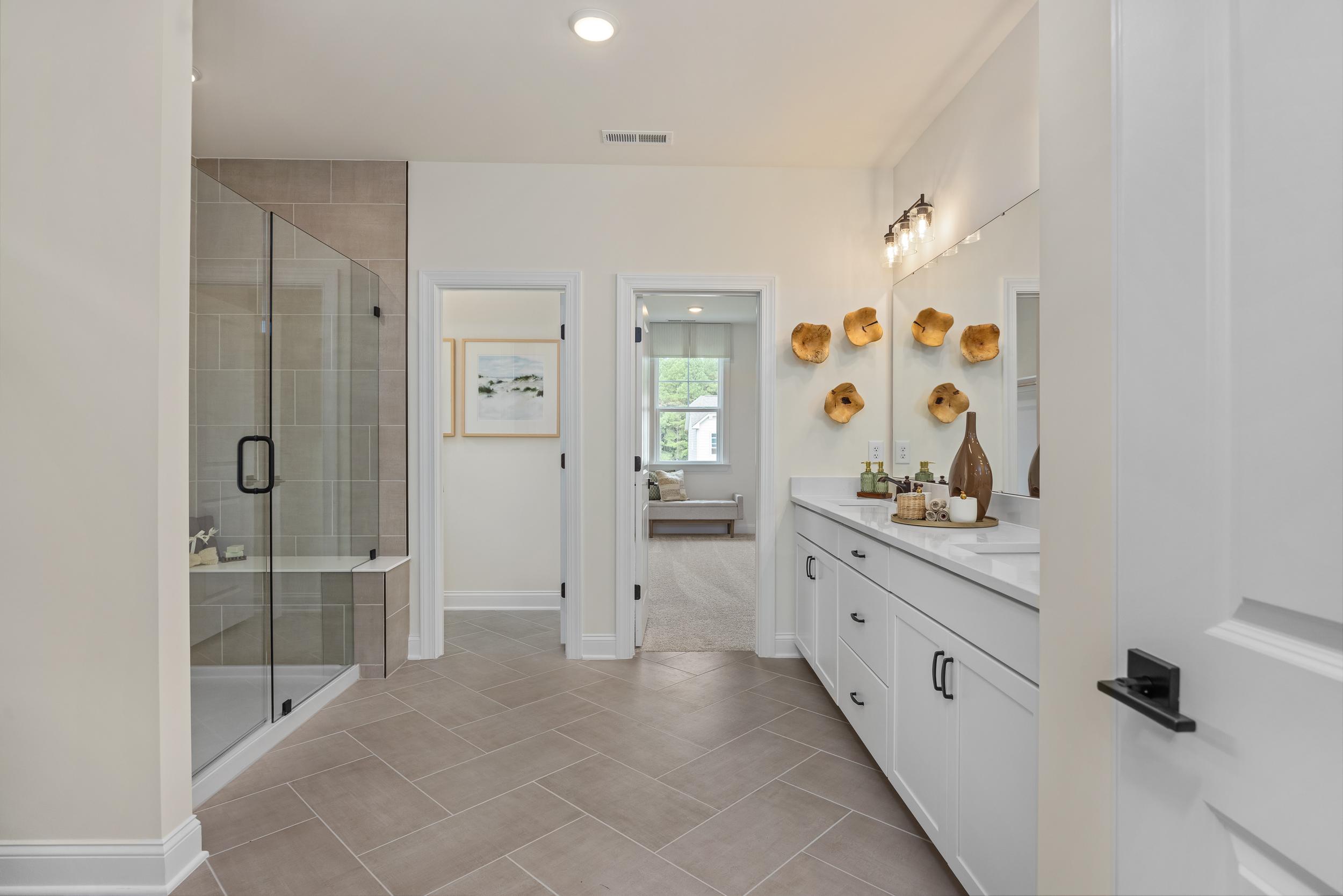 Spacious master bathroom at Laneridge Estates in Raleigh NC by Davidson Homes with glass shower, double white vanity, and herringbone tile floor