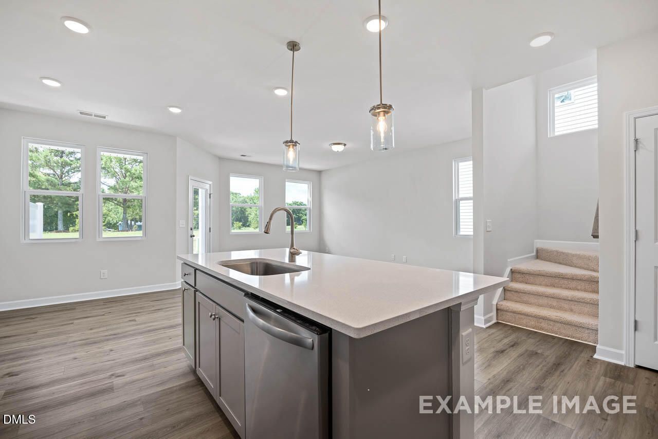 Modern kitchen island with quartz countertops and pendant lighting in The Graham floor plan at Springvale, Fuquay-Varina.