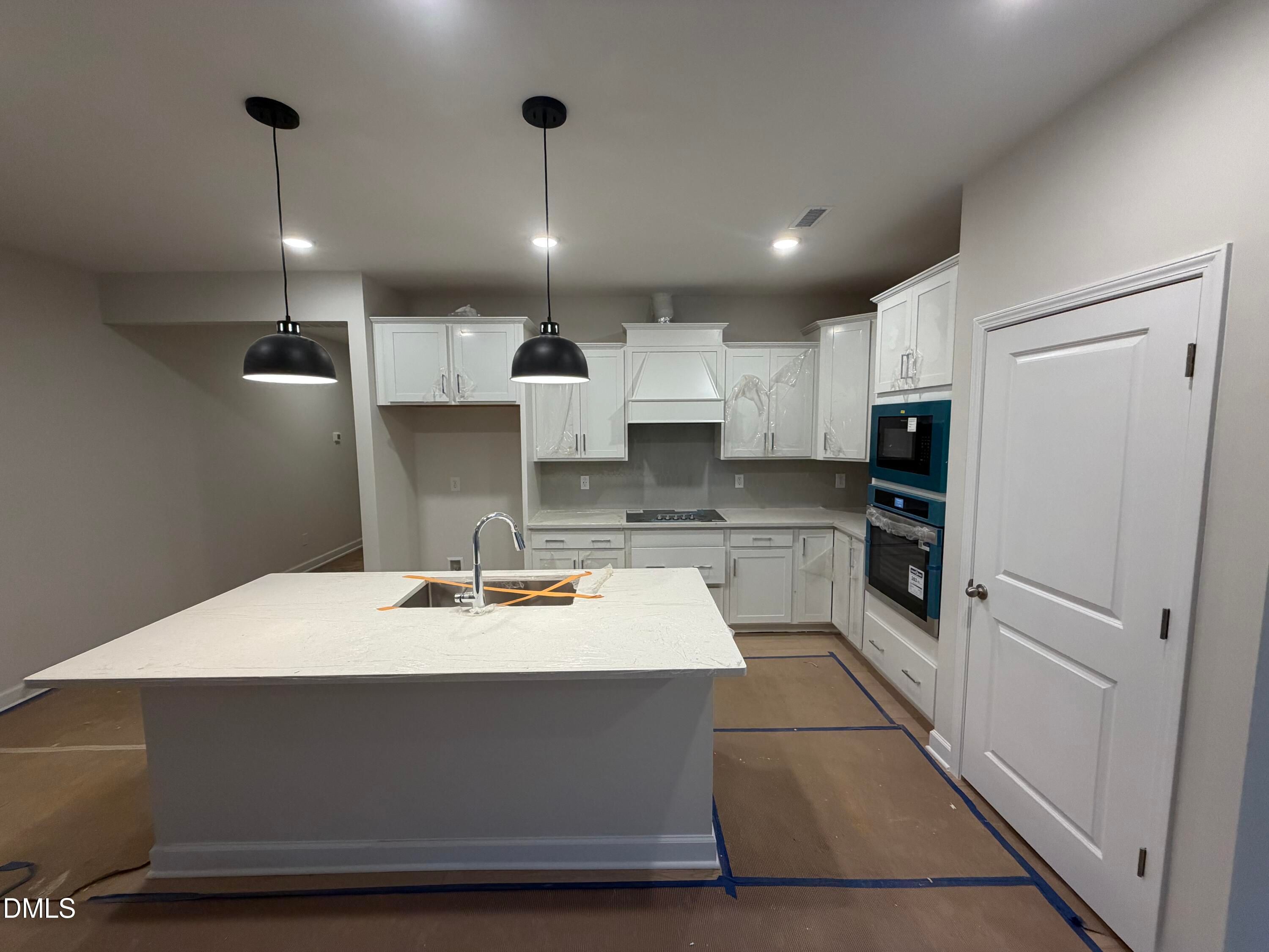 Modern white kitchen with large island sink, pendant lights, and stainless appliances in The Daphne C floor plan, Lillington, NC
